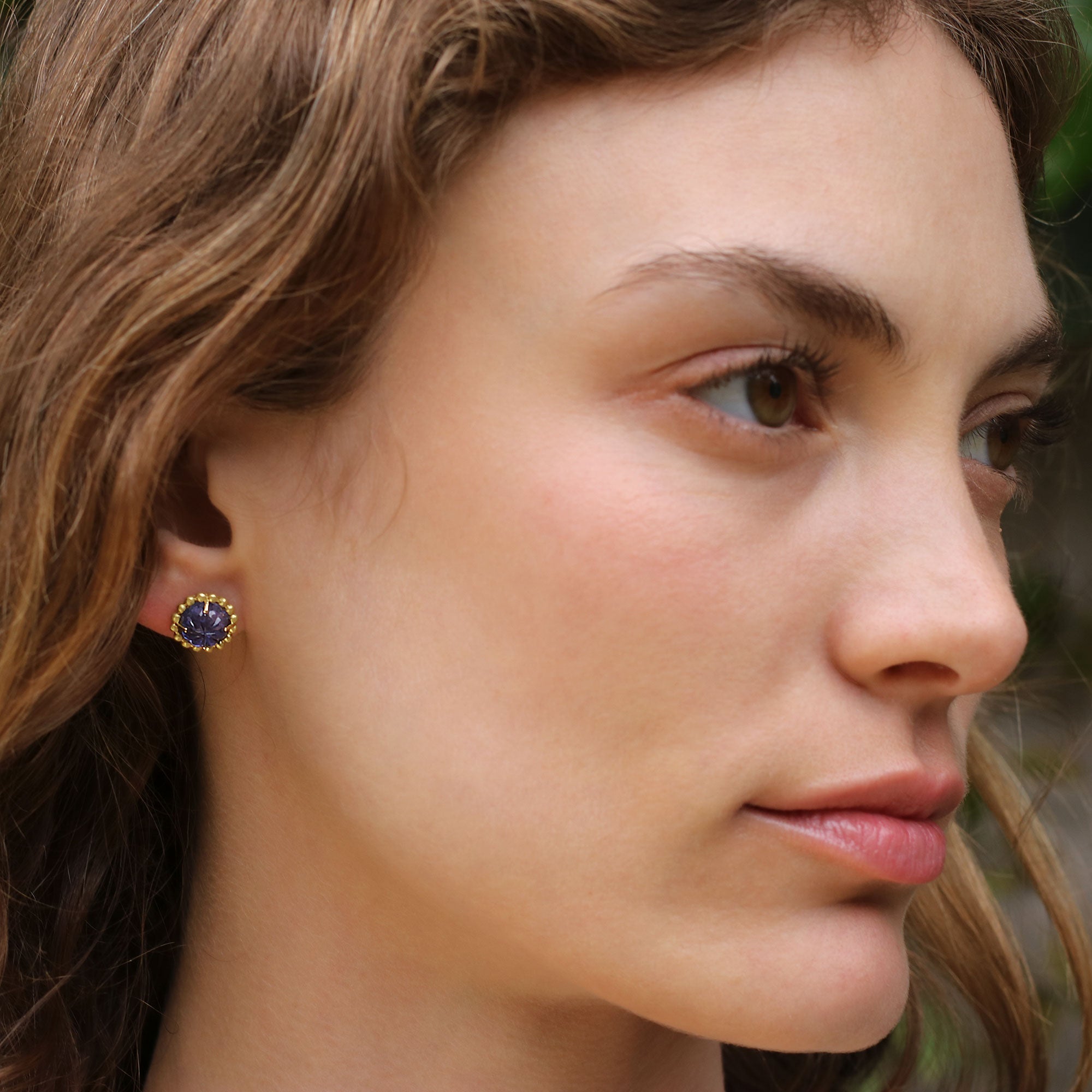 Model wearing 18k gold stud earrings featuring hand-carved tanzanite flower blossoms with a beaded surround from Los Angeles fine jewelry designer Brooke Gregson