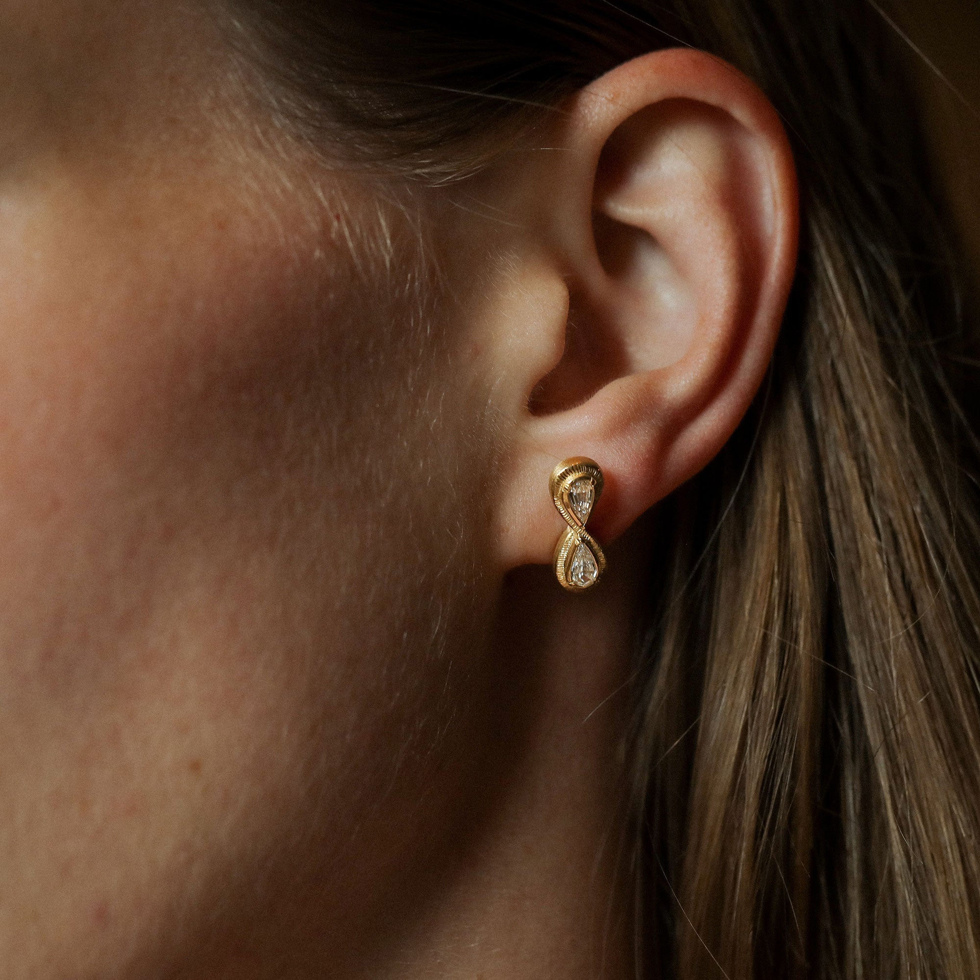 Close up of model wearing 18k gold white diamond double teardrop stud earrings with hand engraving from Los Angeles jewelry designer Brooke Gregson