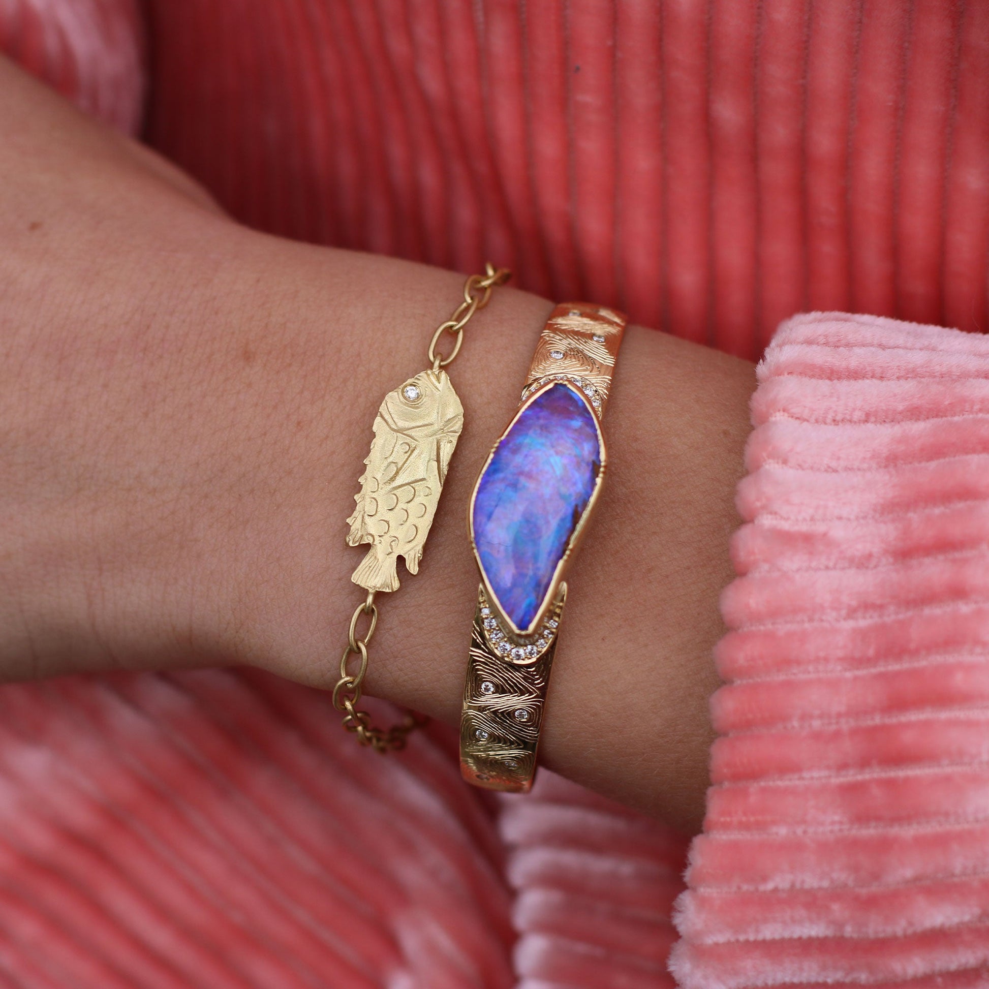 Gold bracelet with fish design and diamond eye stone on wrist against pink fabric background