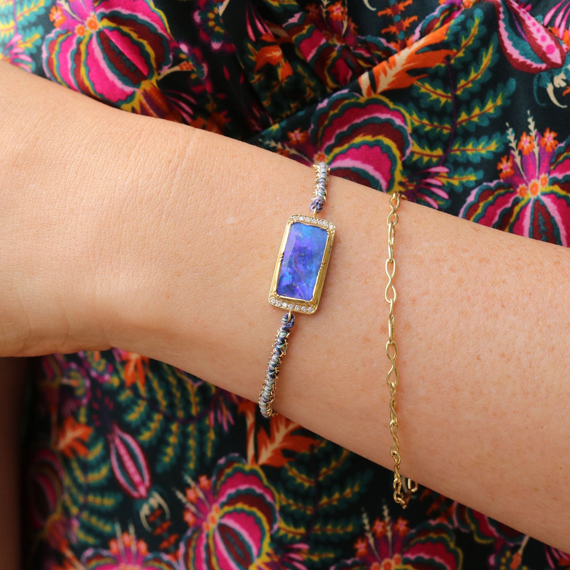 Gold bracelet with a boulder opal gemstone on a wrist against a colorful floral background