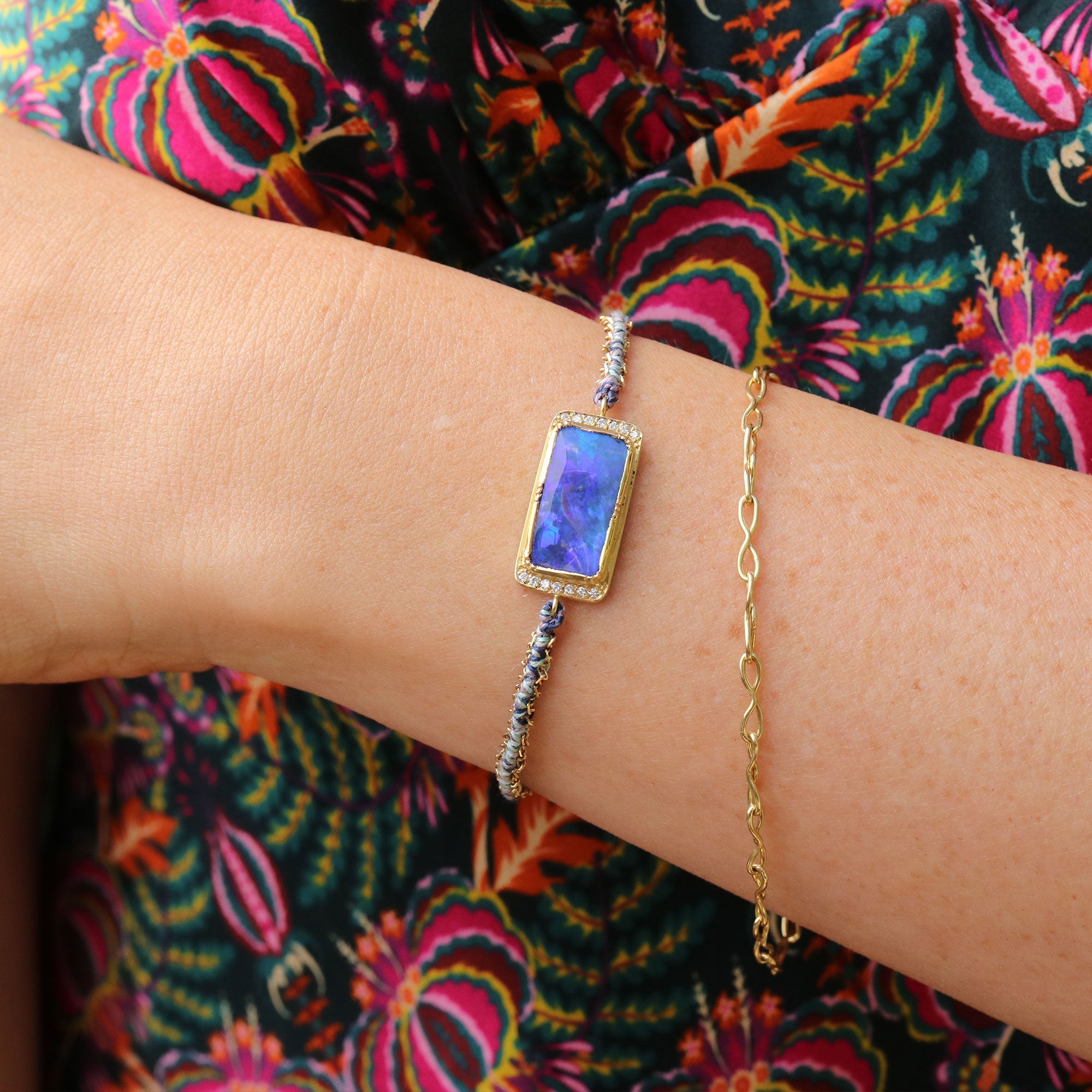 Gold bracelet with a boulder opal gemstone on a wrist against a colorful floral background