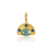 A gold pendant featuring a semi-circular sunburst design with a central round light blue aquamarine stone and three smaller star-shaped blue sapphire stones, shown on a white background with a soft reflection below.