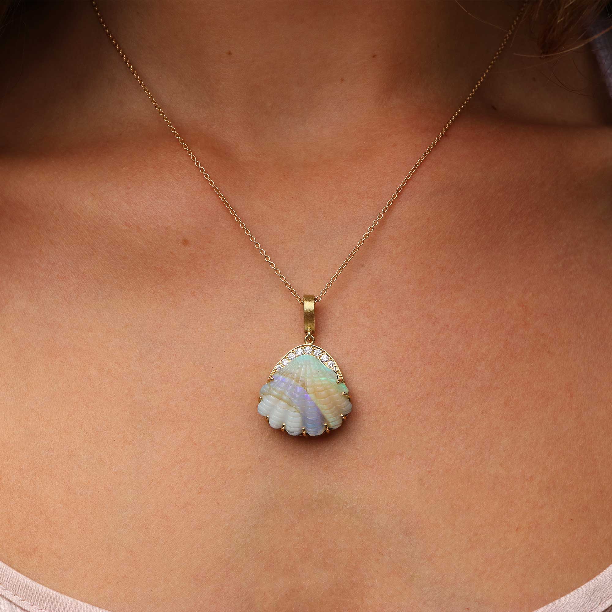 A gold chain necklace with a scallop-shaped pendant featuring iridescent opal shell-like segments in pale blue, lavender, and cream, bordered by small diamond stones, shown worn on a model's neck.