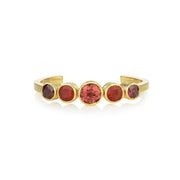 a gold hand engraved cuff with fire opal garnets and tourmalines on a white background.