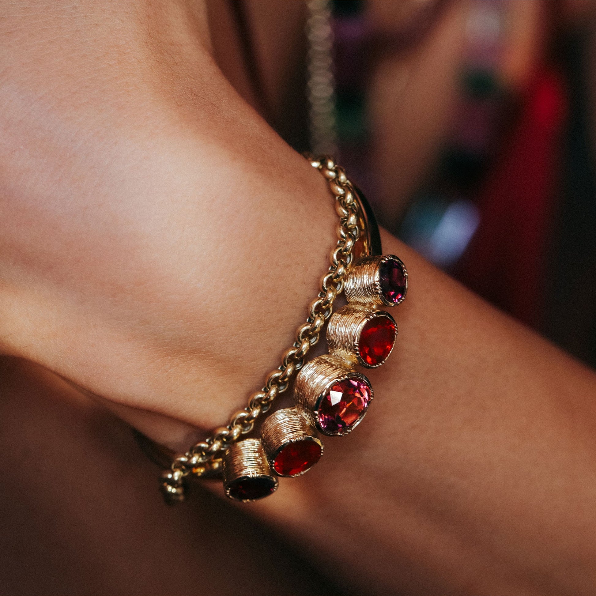Gold bracelet with tourmaline gemstones on a wrist against a blurred background