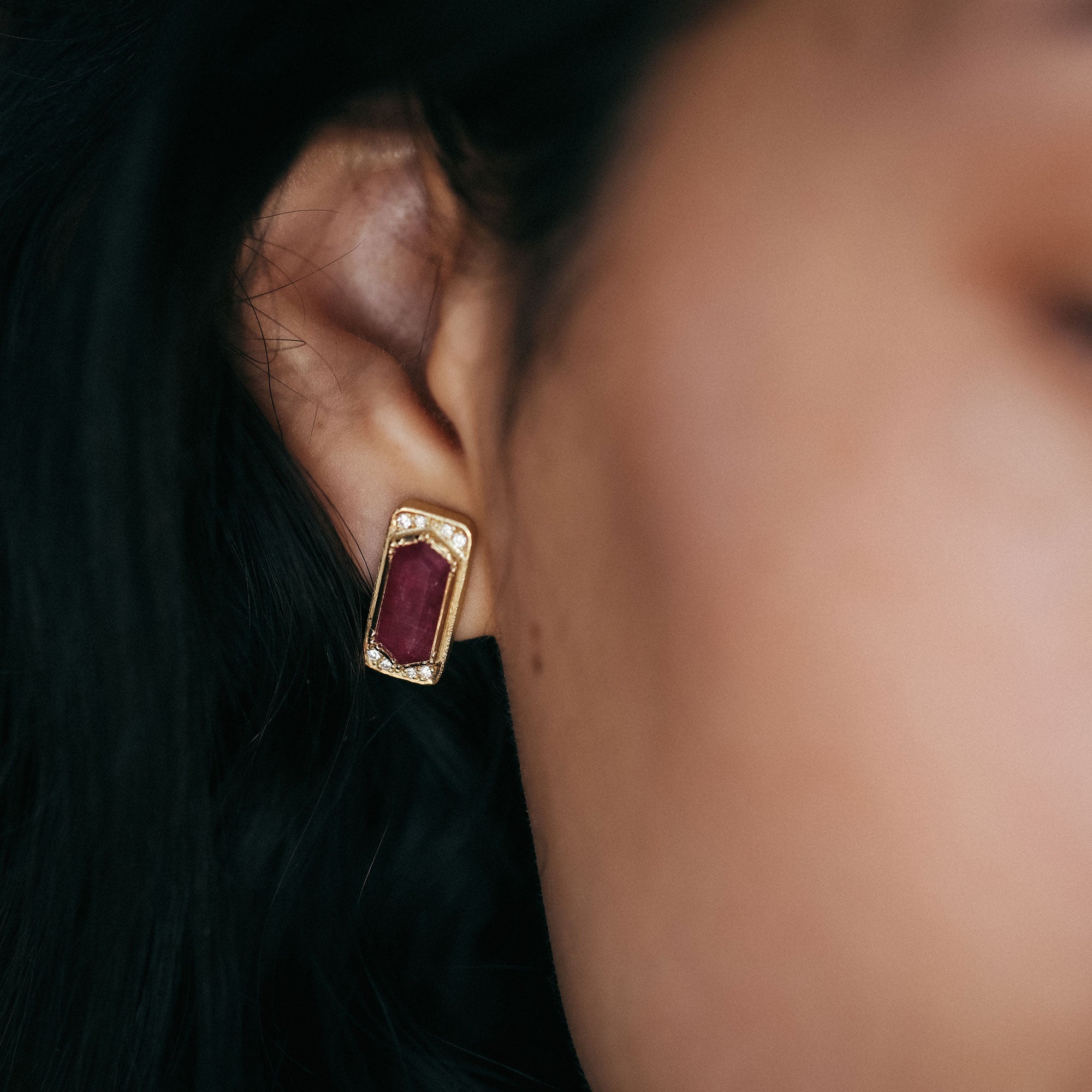 Close-up of an ear wearing a gold earring with a red ruby gemstone.