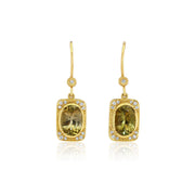 A pair of gold drop earrings featuring rectangular yellow-green tourmline gemstones surrounded by small diamond stones, shown on a clean white background with a soft reflection below.