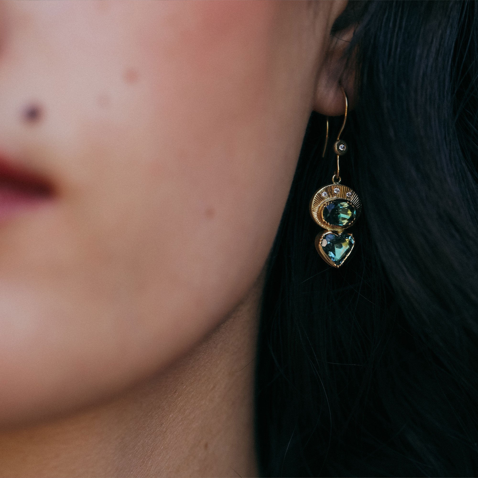 Close-up of a person wearing a gold earring with heart-shaped indicolite tourmaline gemstones.