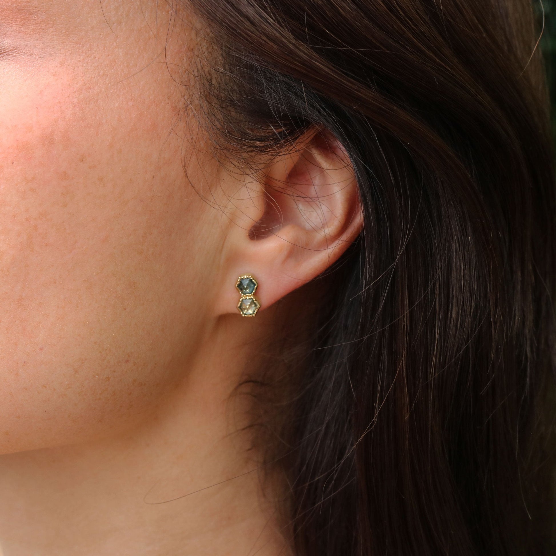 Close-up of an ear wearing a gold earring with montana sapphire gemstones.