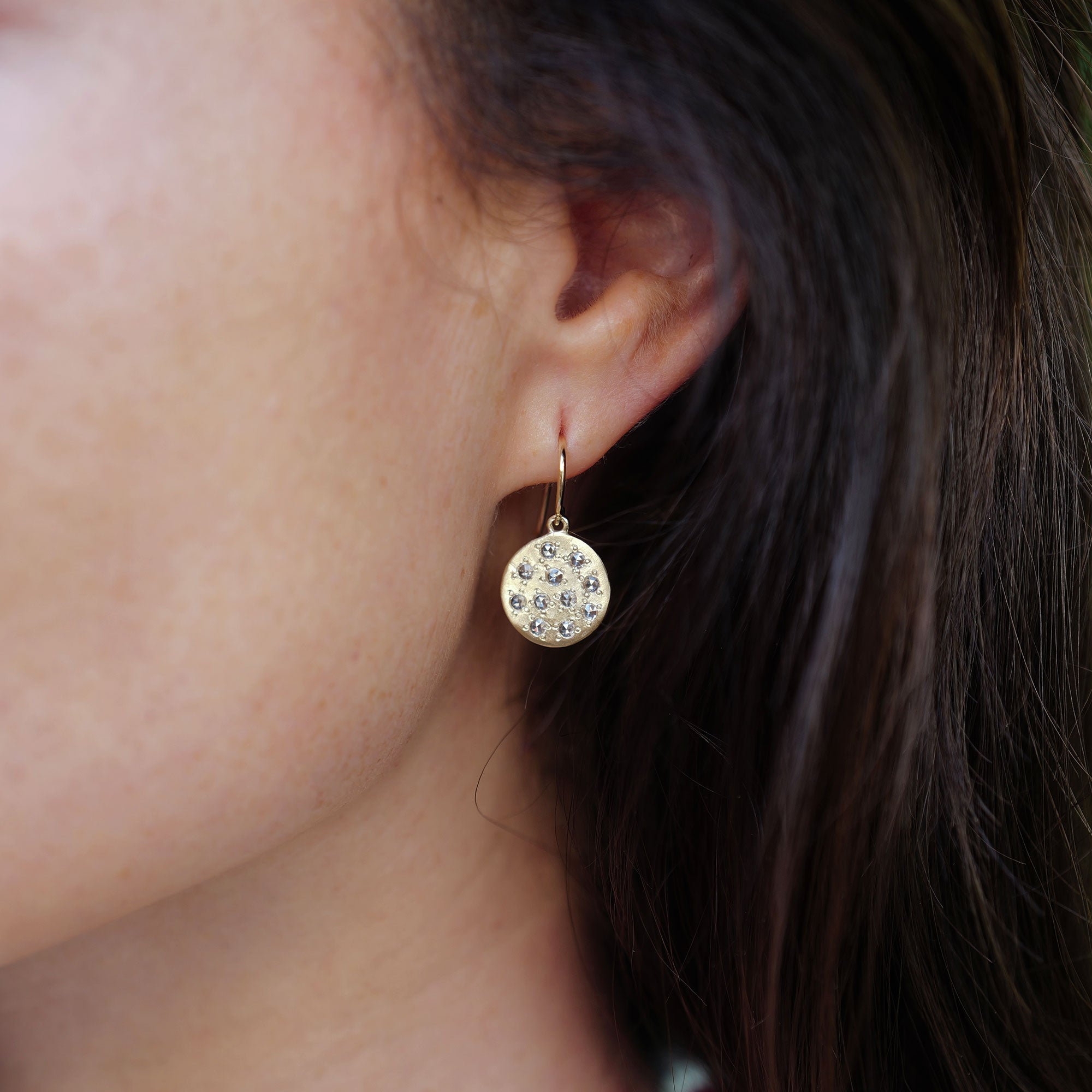 Close-up of an ear wearing a round 18k gold earring with small diamond stones.