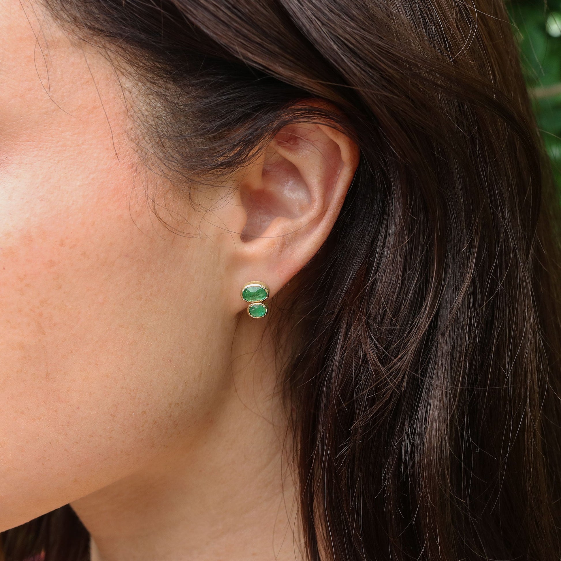 Close-up of an ear wearing green emerald earrings with hair partially obscuring the view.