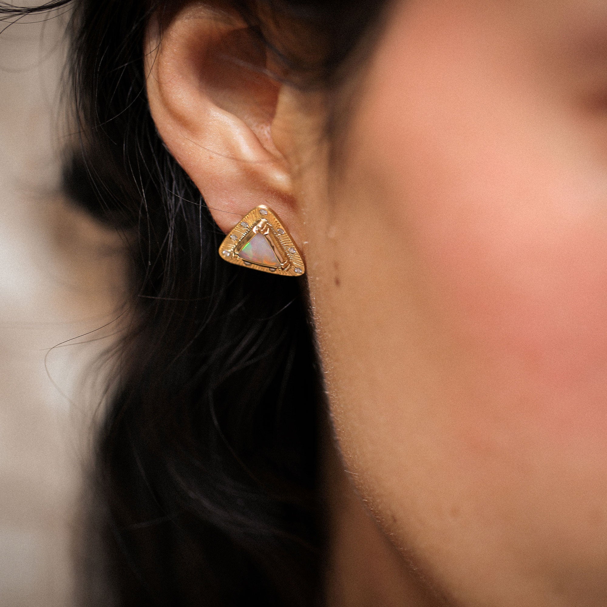 Close-up of a person wearing a gold triangle-shaped earring with a blurred background