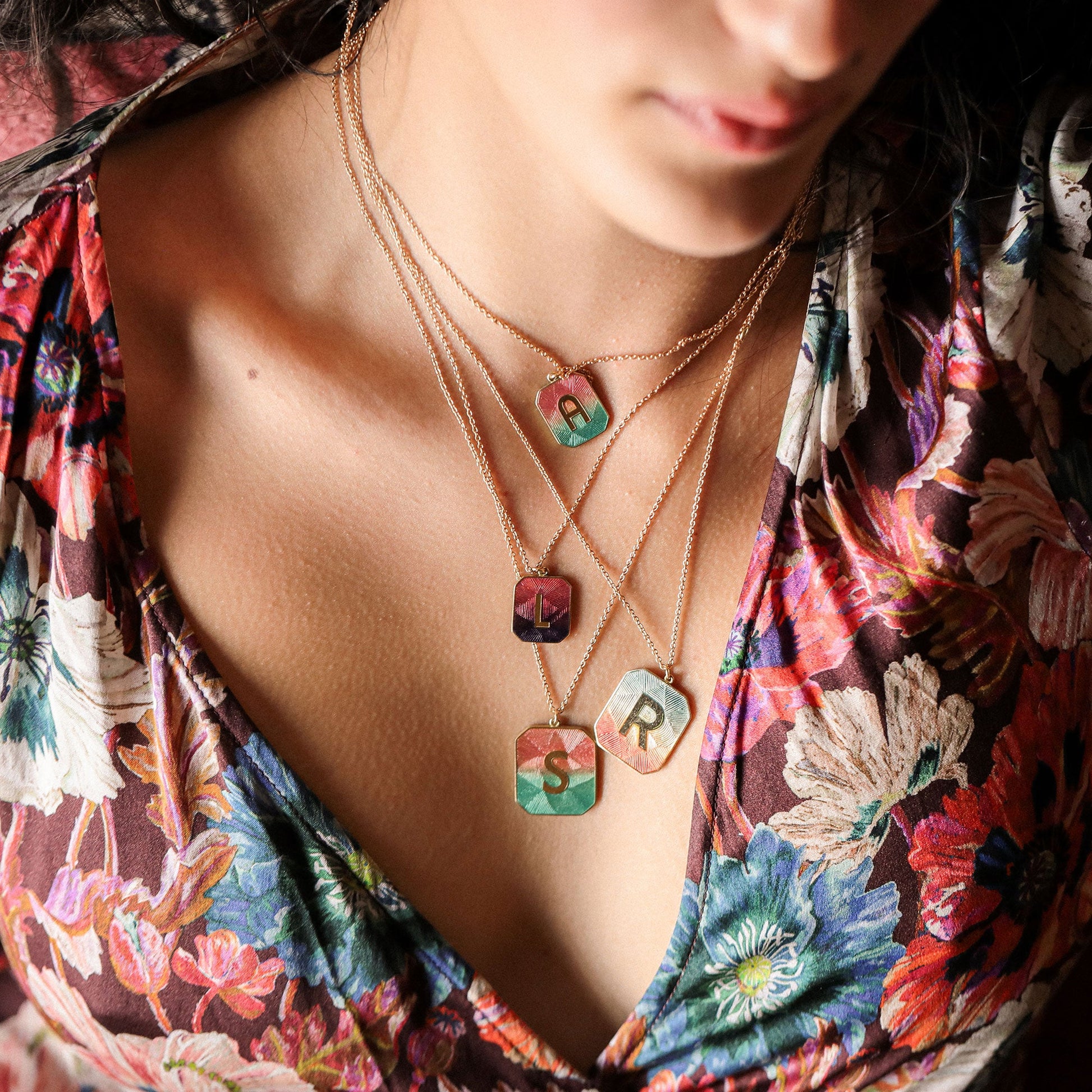 Necklace with colorful pendant letters worn by a person in a floral top