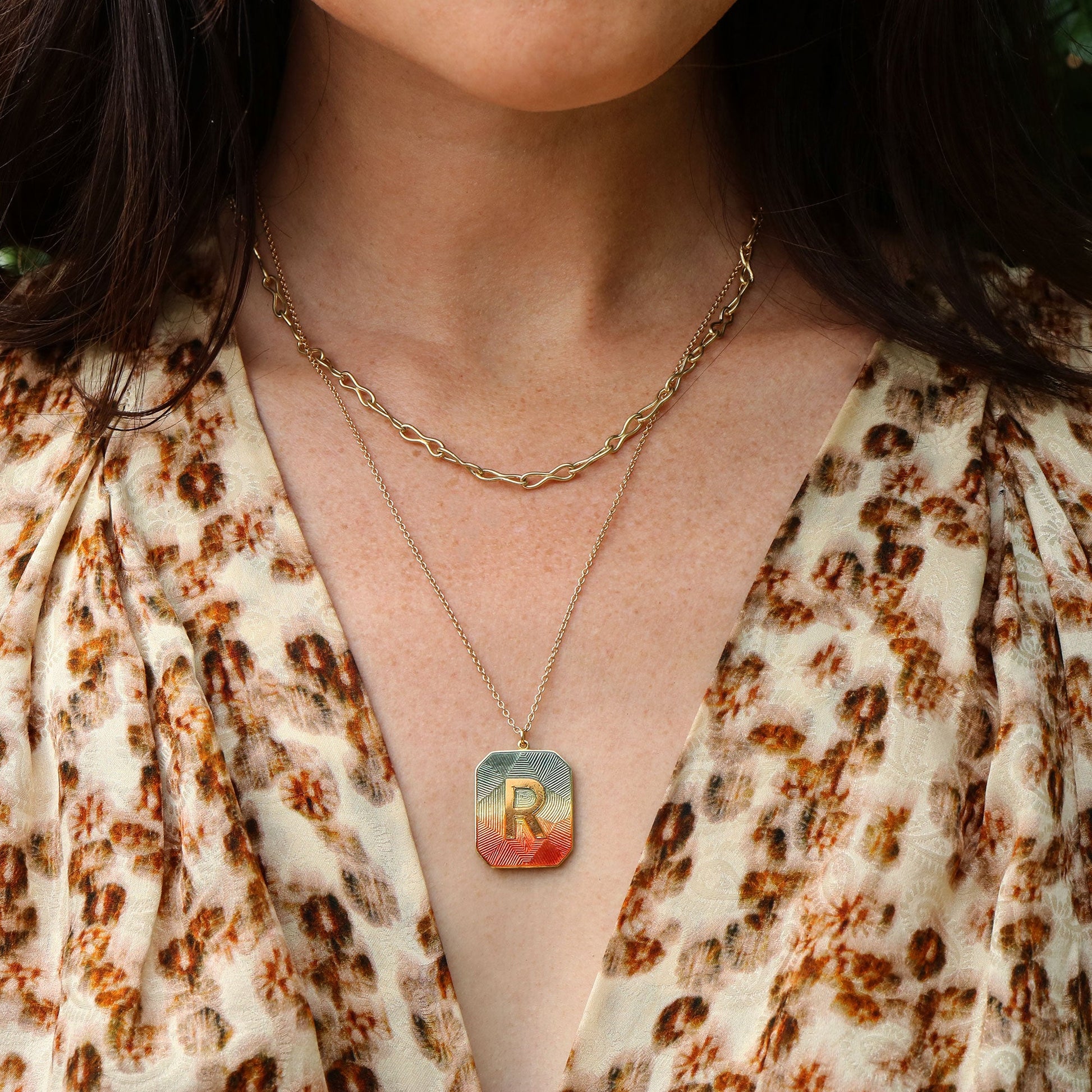 Necklace with an enamel pendant featuring the letter 'R' worn by a person in a floral top.