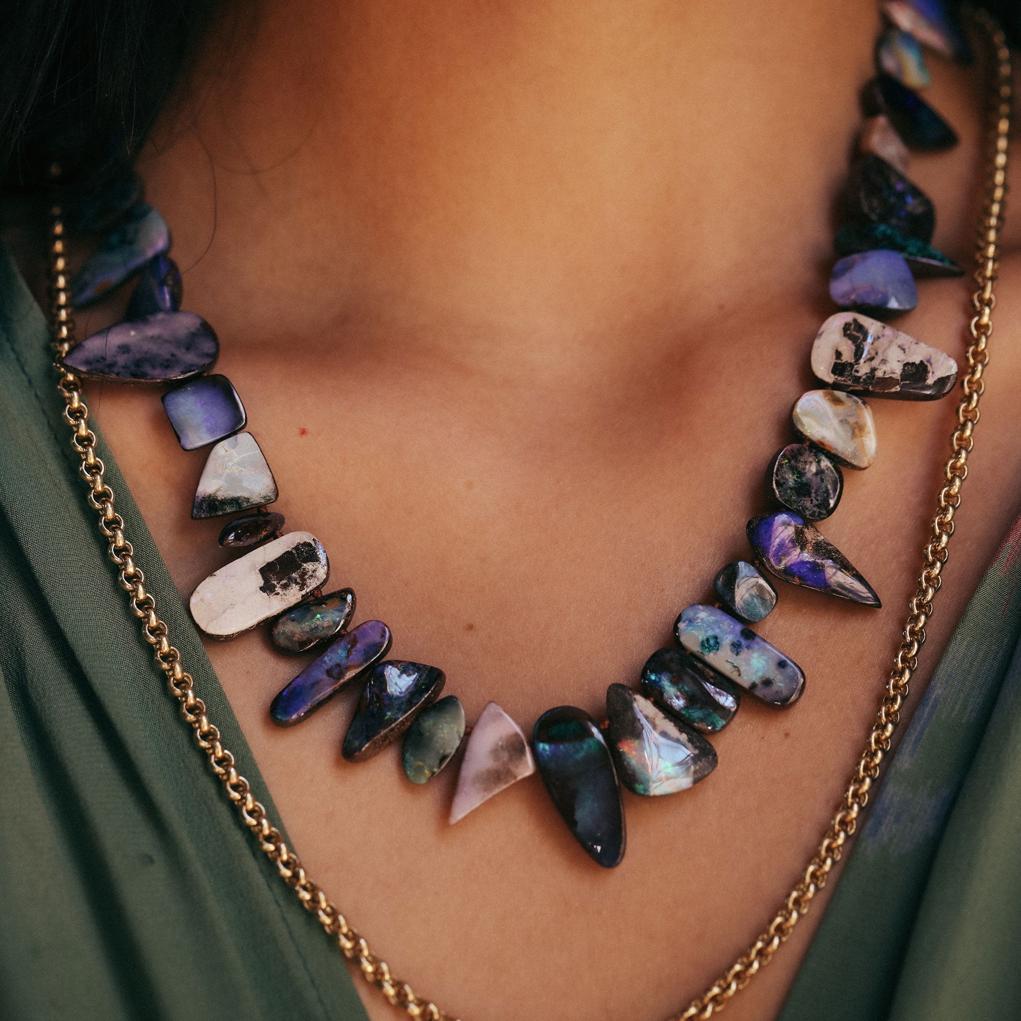 Necklace with multicolored stones and gold chain on a person wearing a green garment.