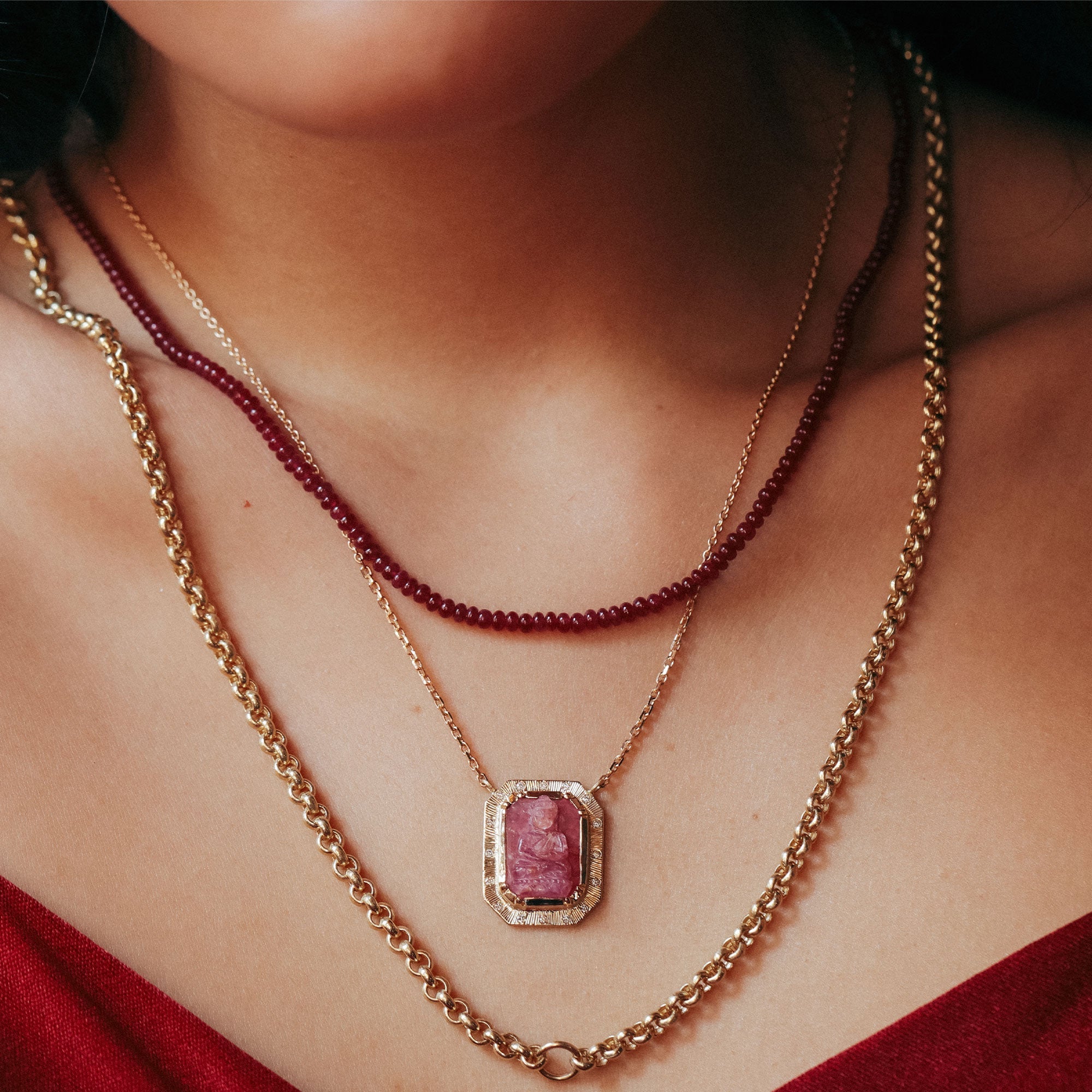 close up of a girl wearing a gold buddah ruby necklace with white diamond accents and hand engraved detailing.