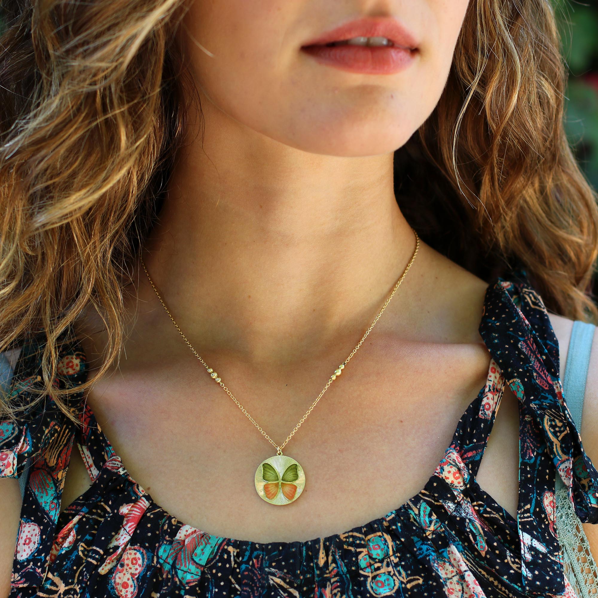 Model wearing Hand made 18k gold hand engraved Enamel butterfly necklace in orange and green enamel ombre. Fine jewelry hand made in London.