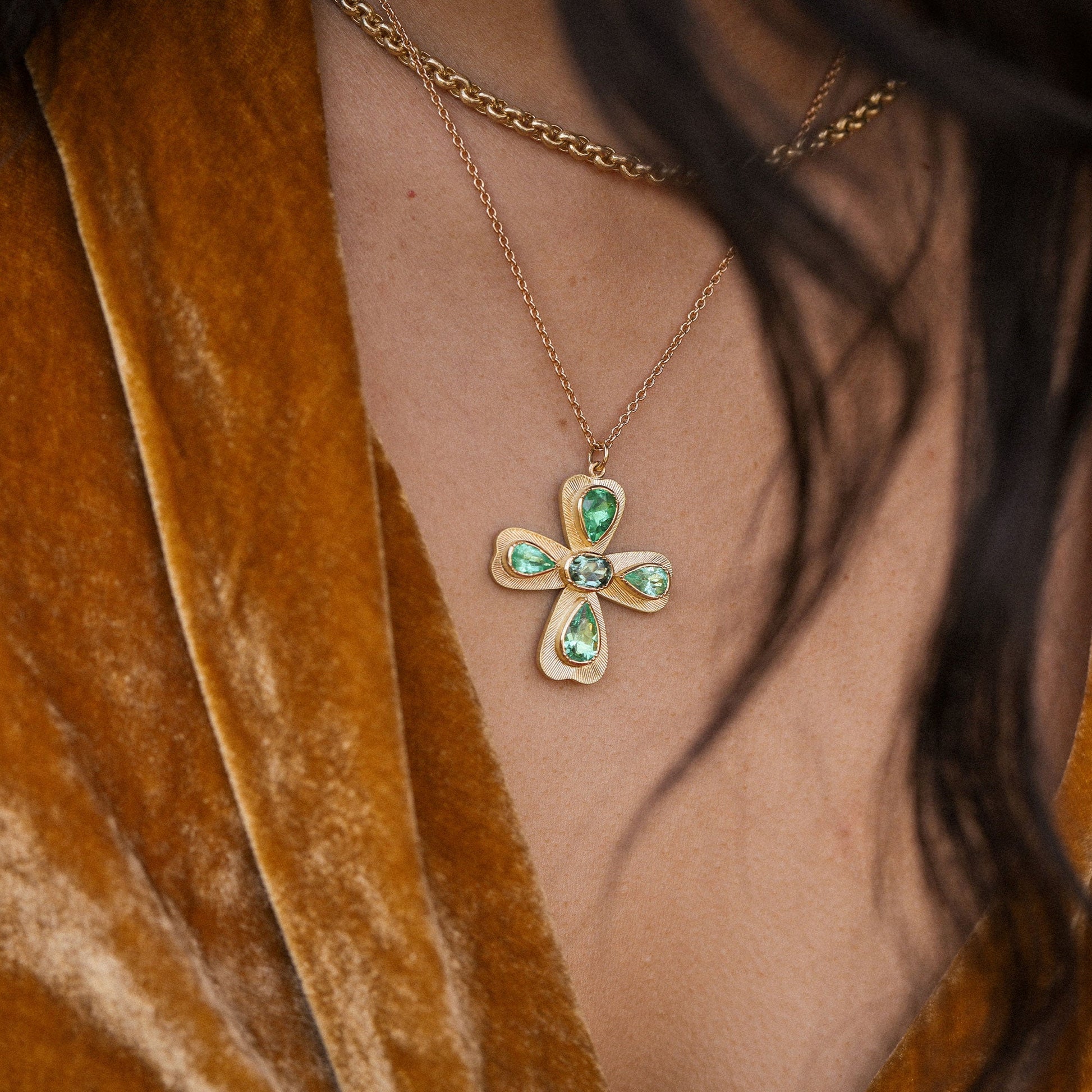 Gold necklace with a green gemstone pendant worn by a person in a brown garment.