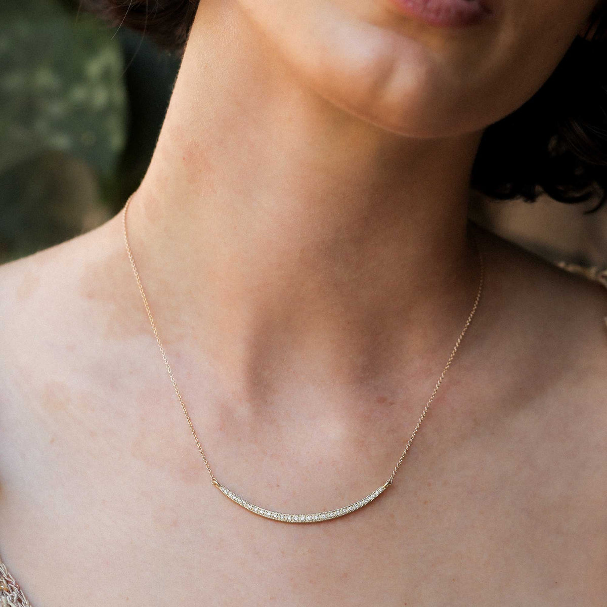 A delicate 18k yellow gold bar necklace with 29 white diamonds designed by brooke gregson worn on a womans bare neck