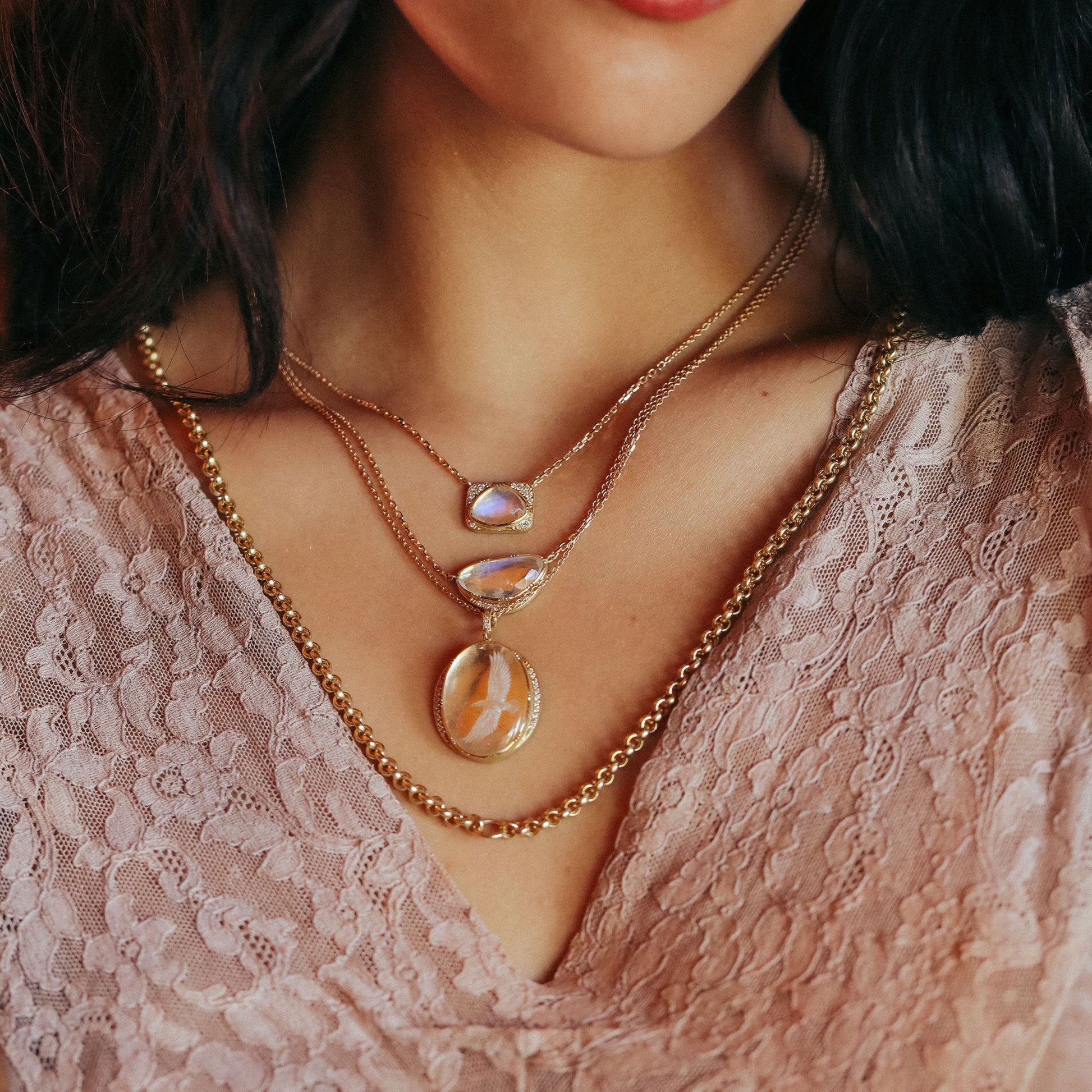 Close-up of a woman wearing a gold necklace with a pendant on a lace garment.