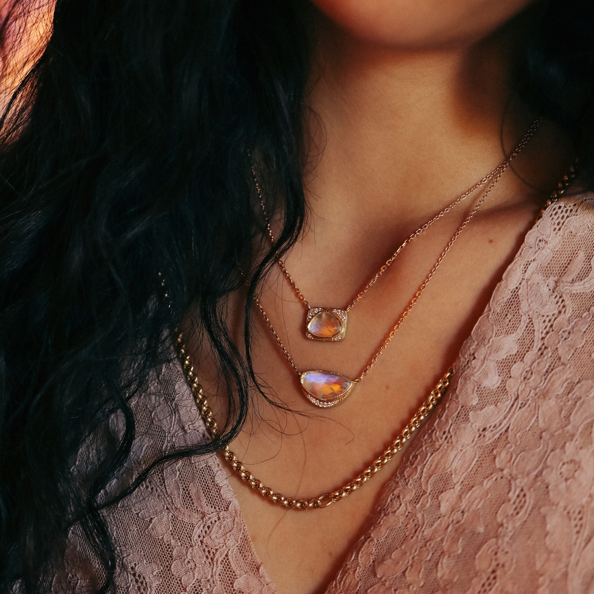 Close-up of a person wearing two gold necklaces with moonstones on a blurred background.