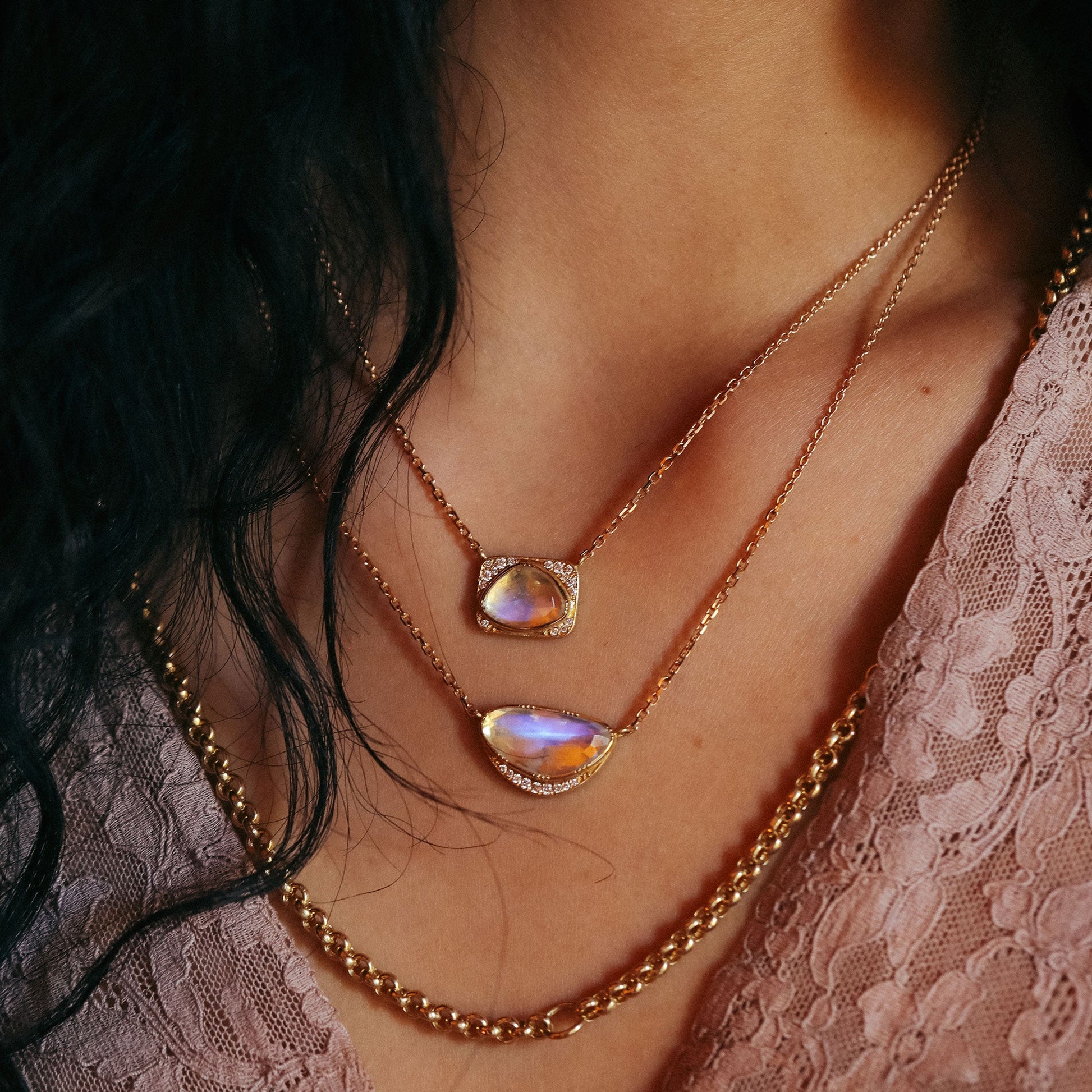 Close-up of a person wearing two gold necklaces with moonstone gemstones.