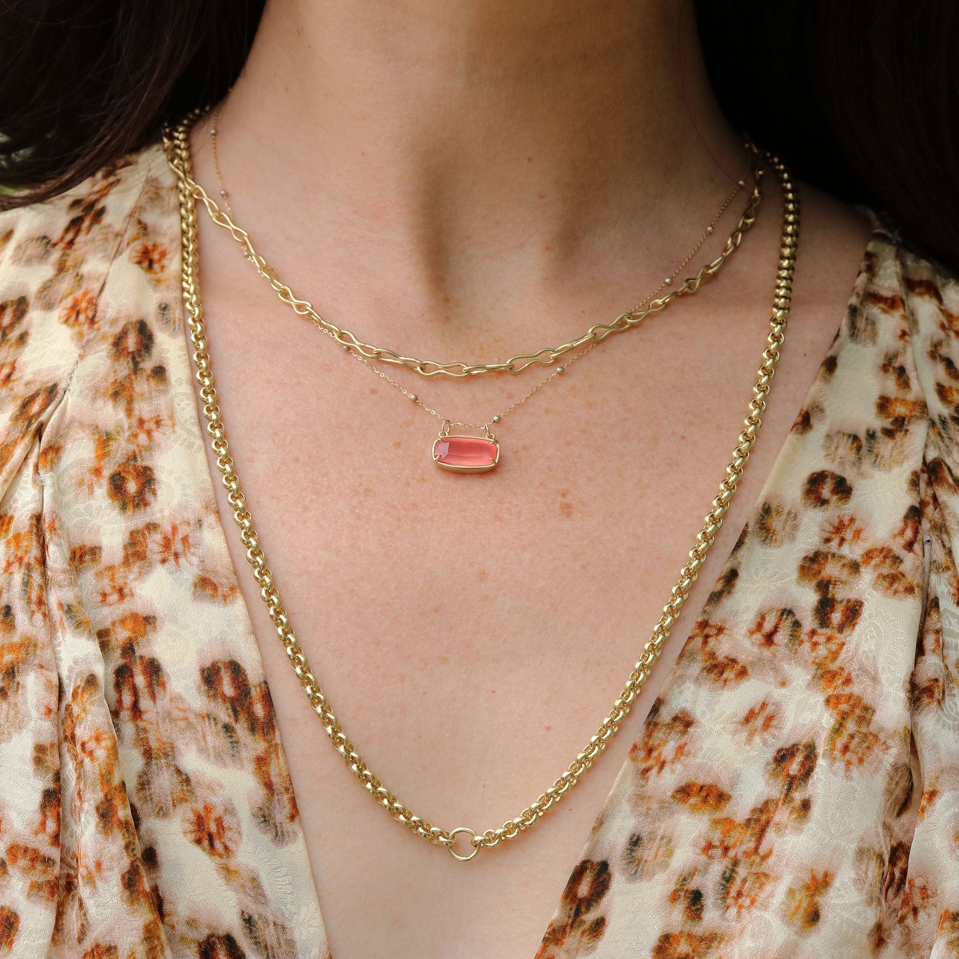 Gold chain necklace with a pink Rhodochrosite pendant worn by a person in a patterned top.