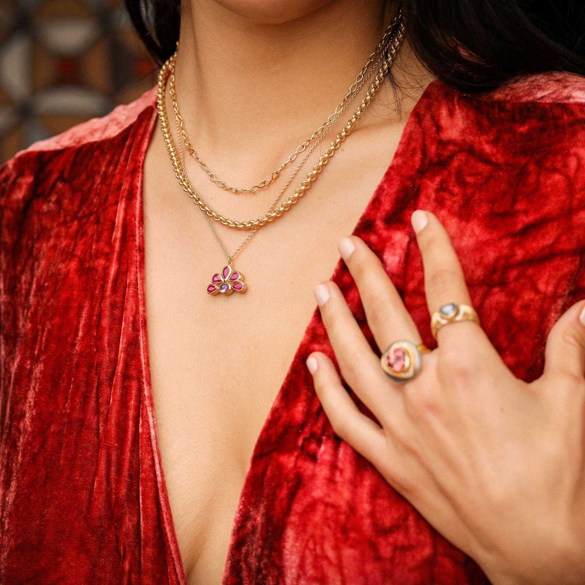 Woman wearing gold jewelry with a butterfly pendant and pink gemstones, against a red velvet background.