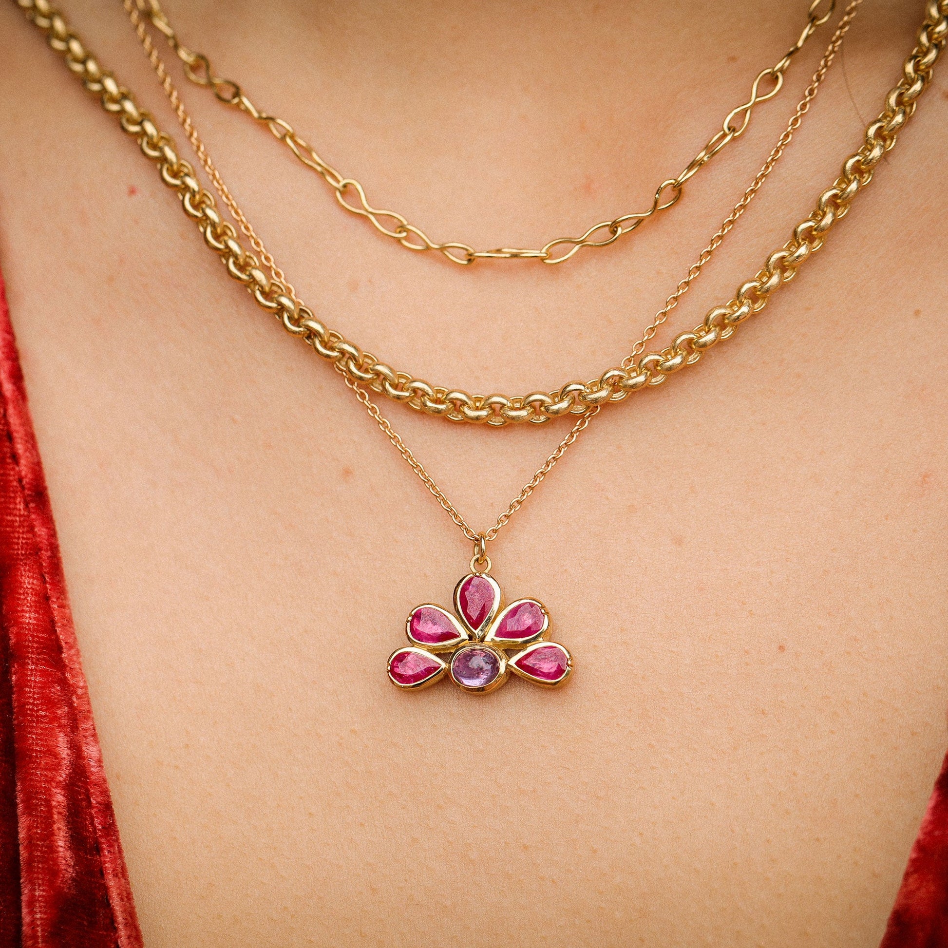 Gold necklace with a floral pendant worn by a person in a red garment.