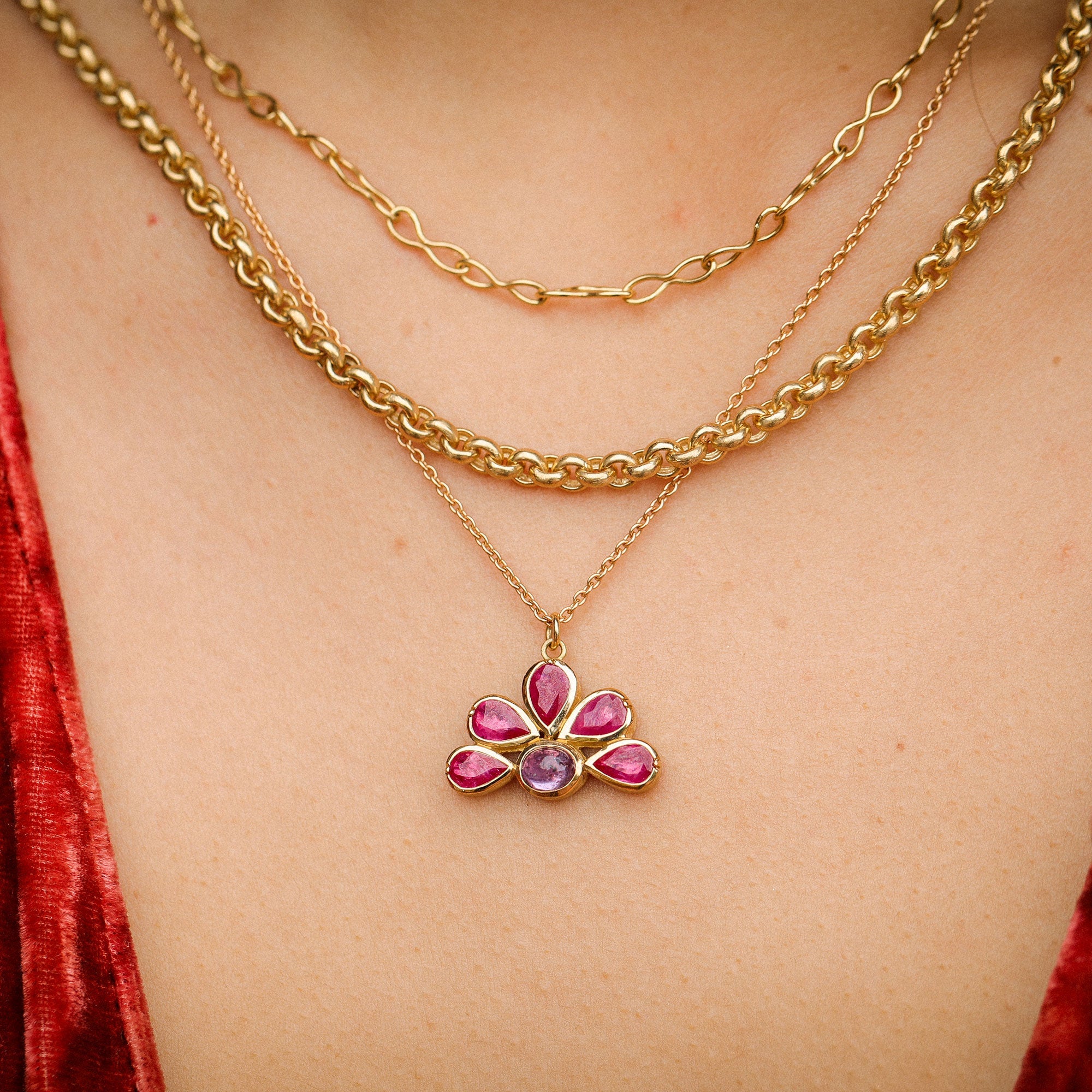 Gold necklace with a floral pendant worn by a person in a red garment.