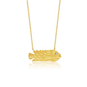 A gold fish-shaped pendant gold necklace with a small diamond gemstone in one eye, suspended from a delicate gold chain against a white background.