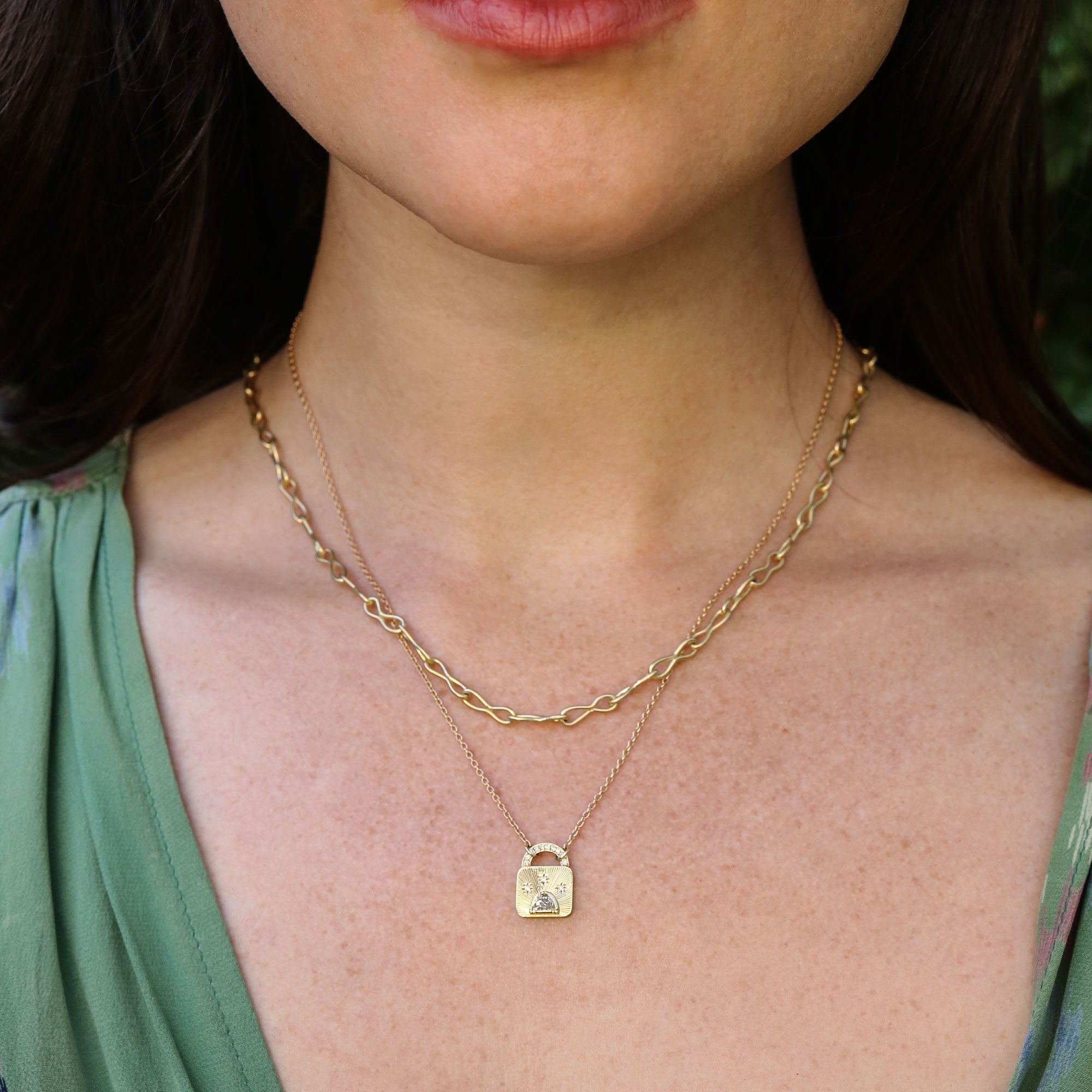 Close-up of a person wearing a gold 18k necklace with a lock-shaped pendant with white diamonds.