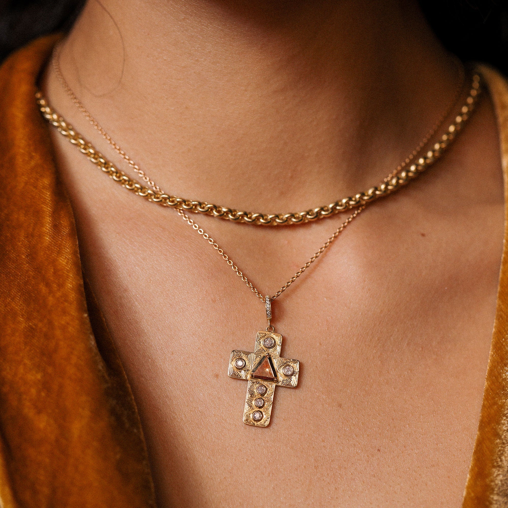 Gold chain necklace with a cross pendant on a person wearing a brown top.
