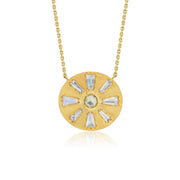 A gold circular pendant necklace featuring a sunburst design with clear baguette-cut diamond stones and a central round pale green diamond gemstone, suspended from a delicate gold chain against a white background.