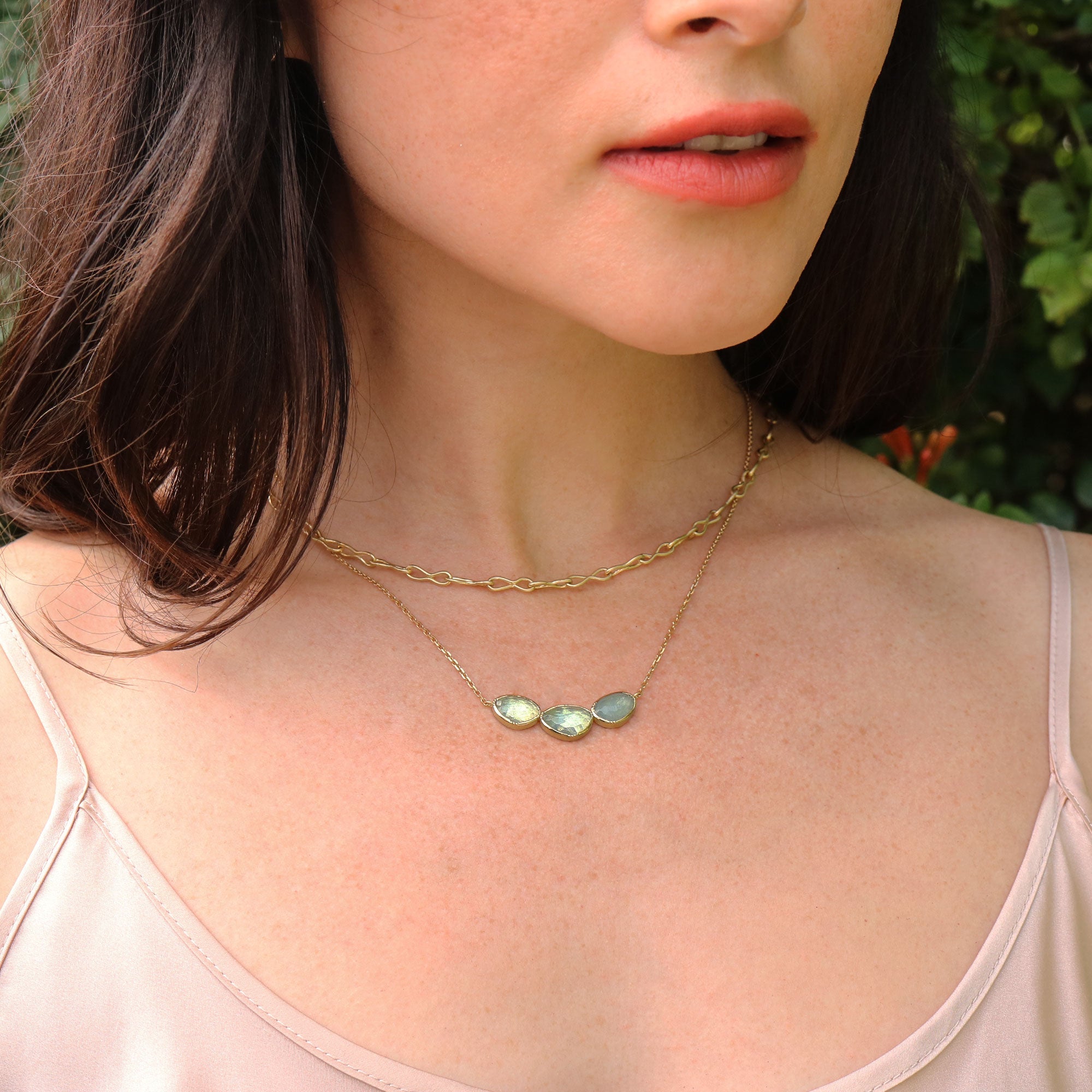 Close-up of a woman wearing a gold necklace with three aquamarine gemstones, outdoors.