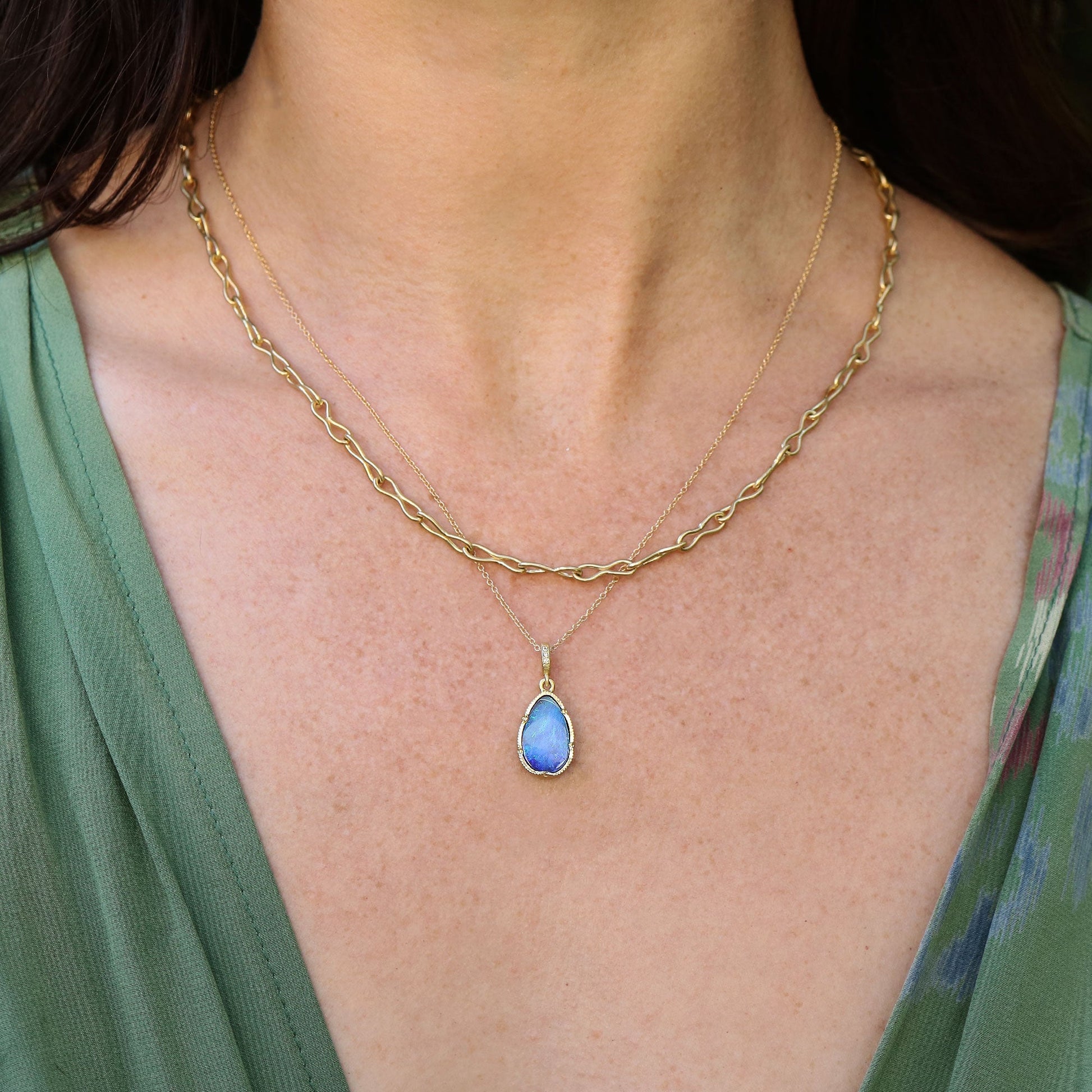 Gold necklace with a blue boulder opal pendant worn by a person in a green top.