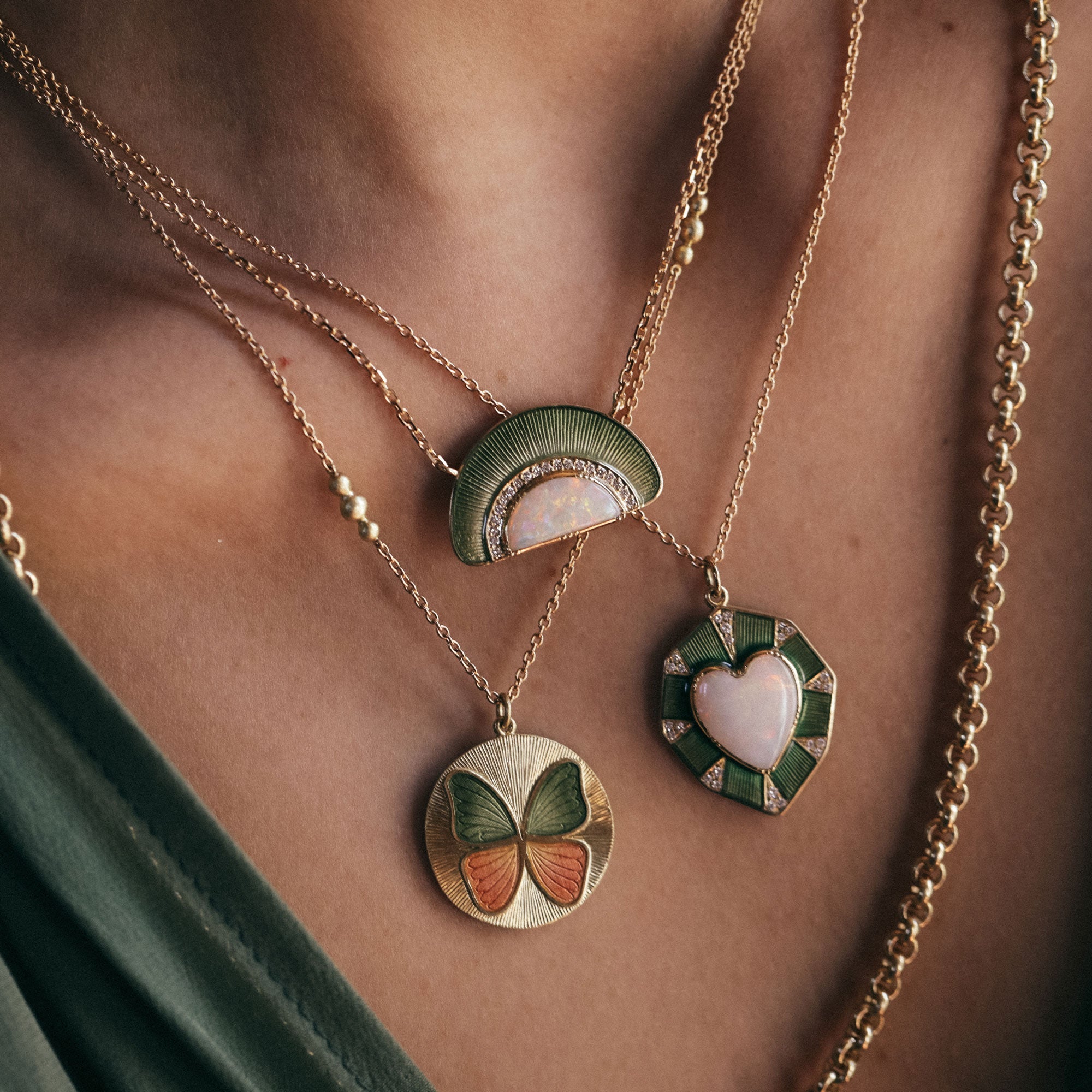 Close-up of a person wearing three gold necklaces with colorful opal and enamel pendants.