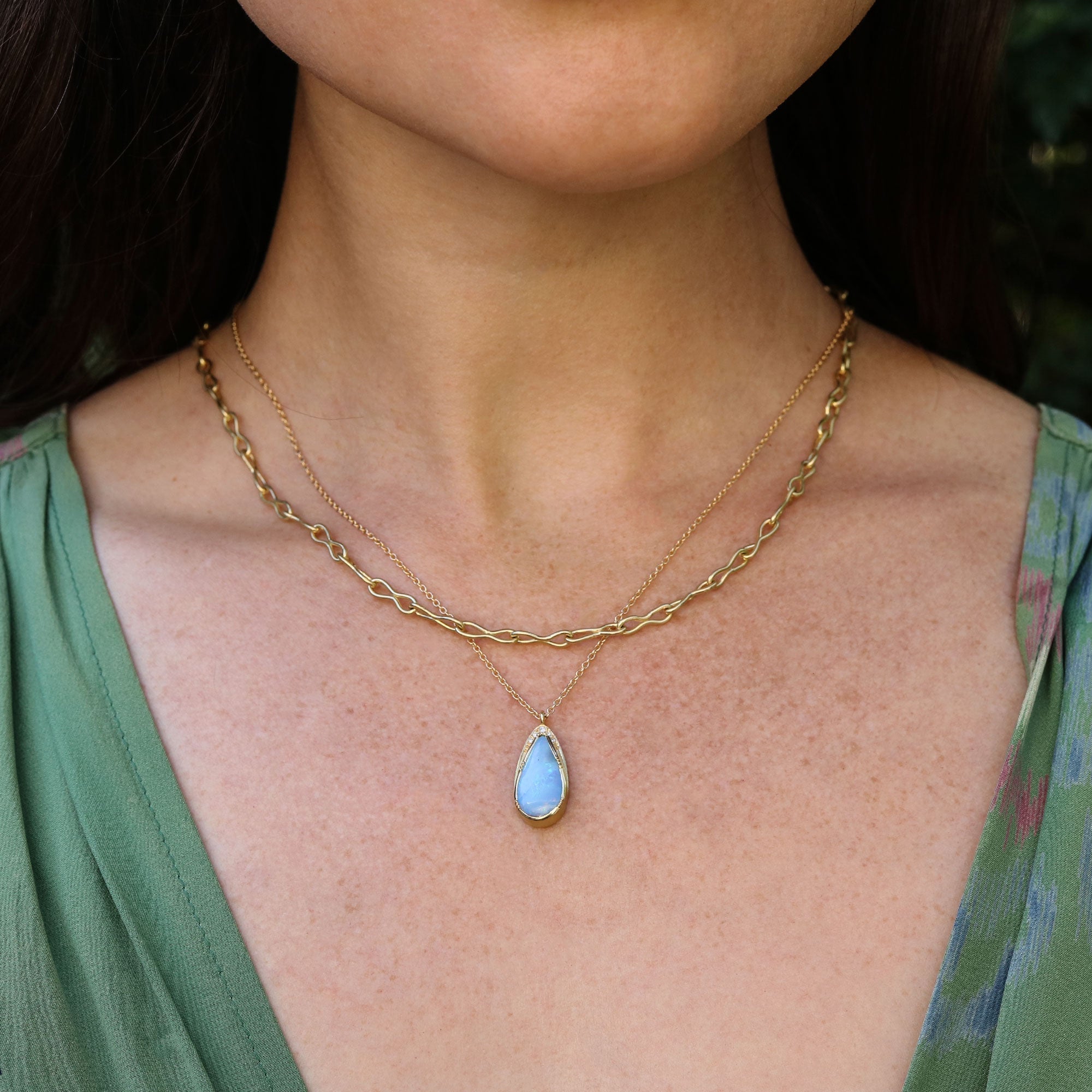 Girl wearing an 18k gold necklace with boulder opal pendant and white diamond halo by Brooke Gregson.