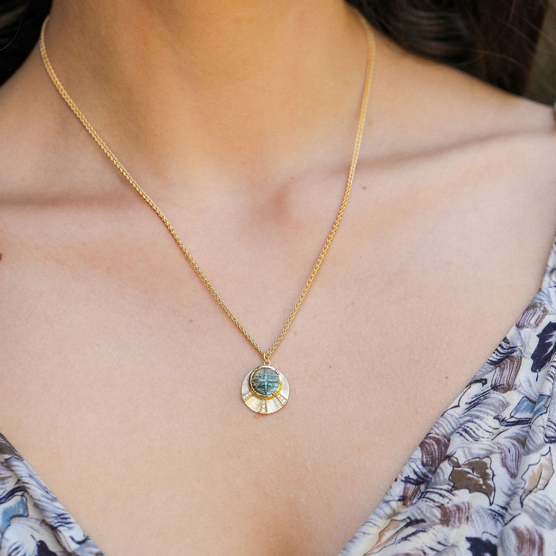close up of neck wearing an 18k gold necklace with hand engraving and a compass chaped labradorite stone with pave white diamonds