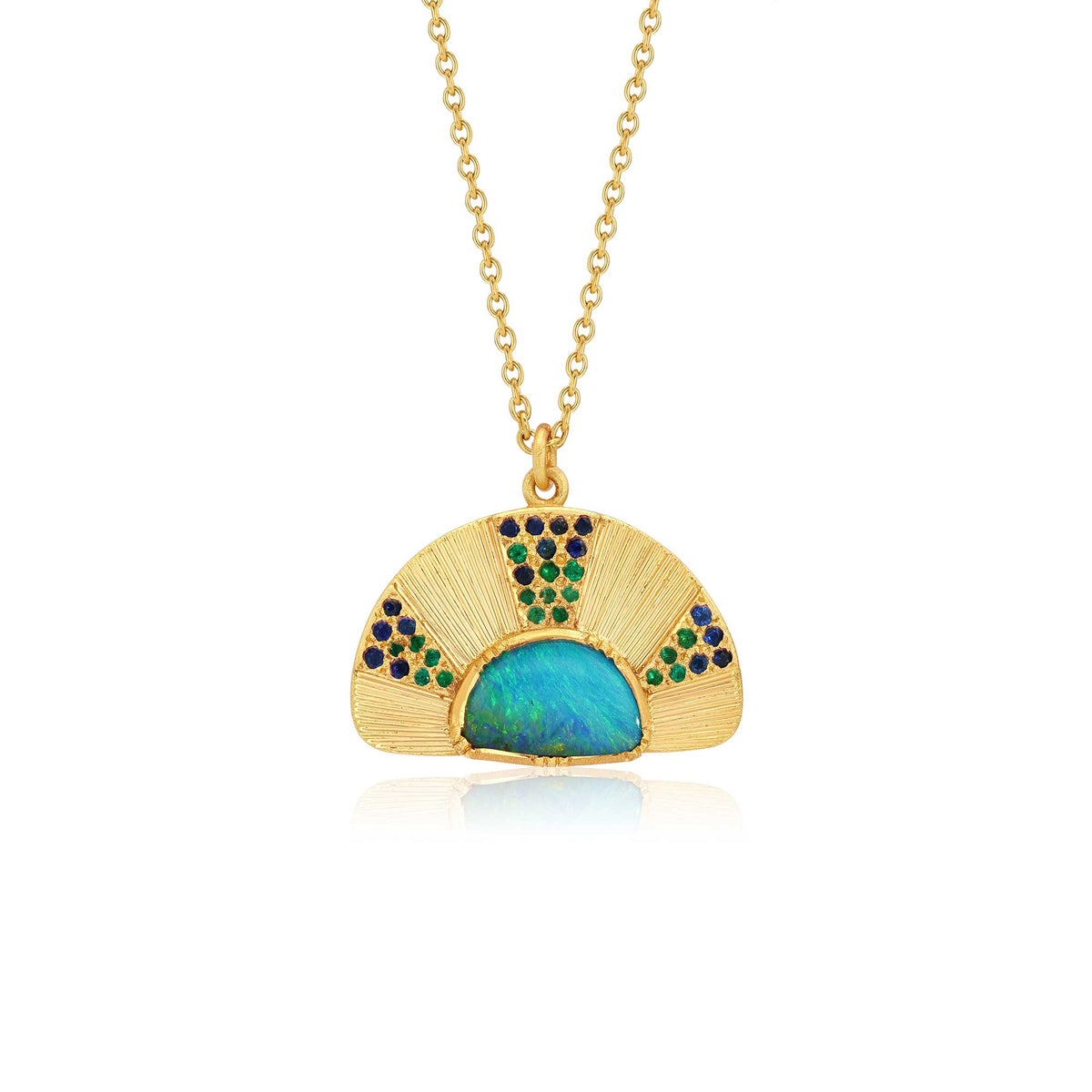 An 18k yellow gold pendant necklace featuring a fan-shaped design with a central iridescent blue-green opal and small emerald and sapphire gemstone accents with hand engraving, shown on a white background with a soft reflection. By jewelry designer Brooke