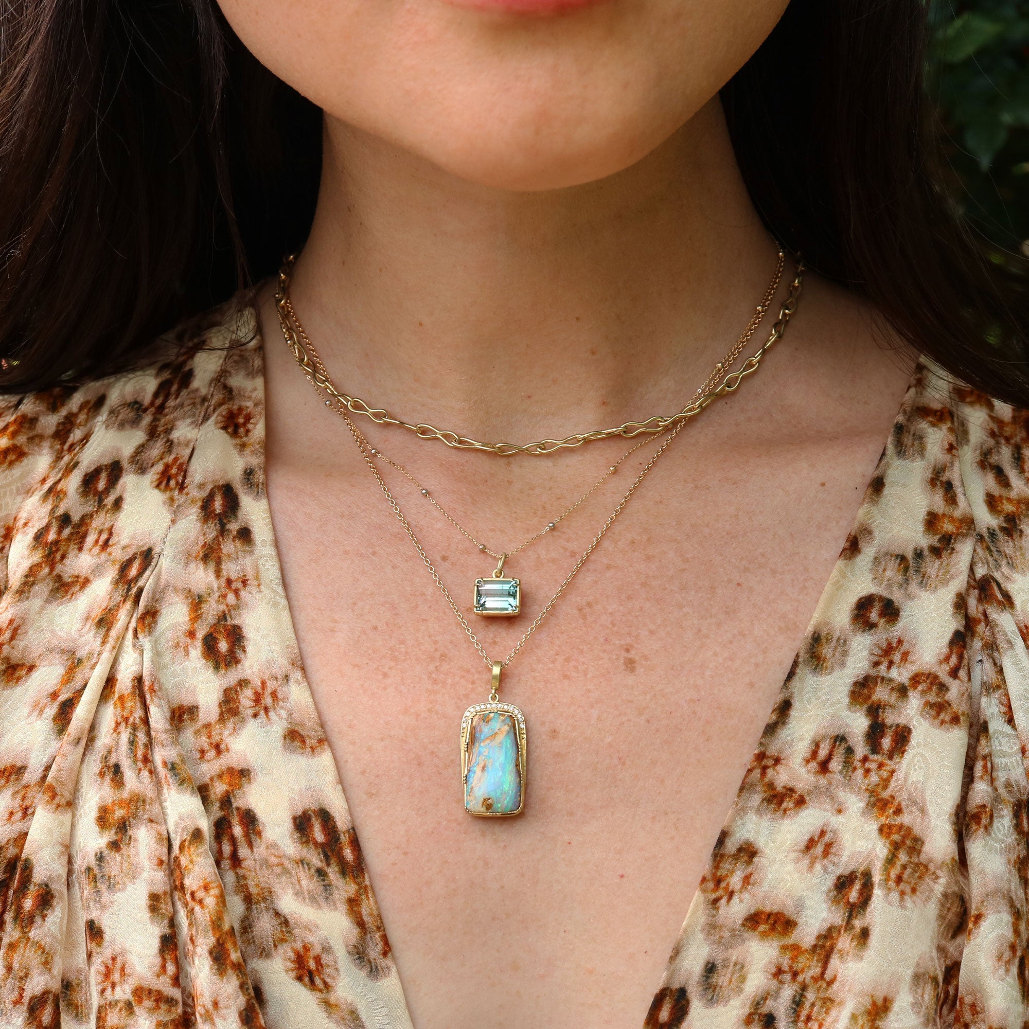Close-up of a person wearing two gold necklaces with fossilised wood opal pendants.