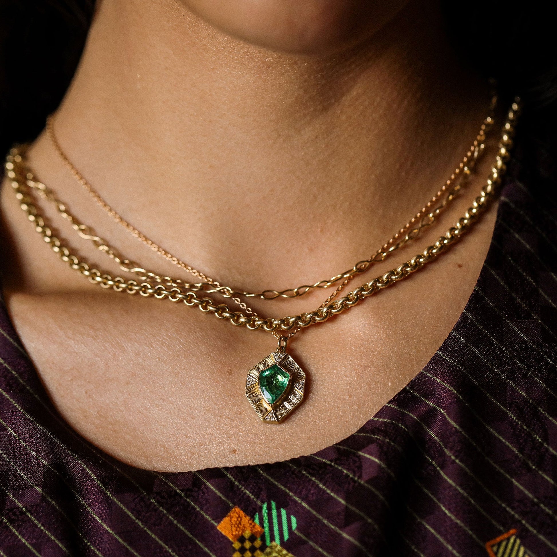 Close-up of a person wearing a gold necklace with a green gemstone pendant.