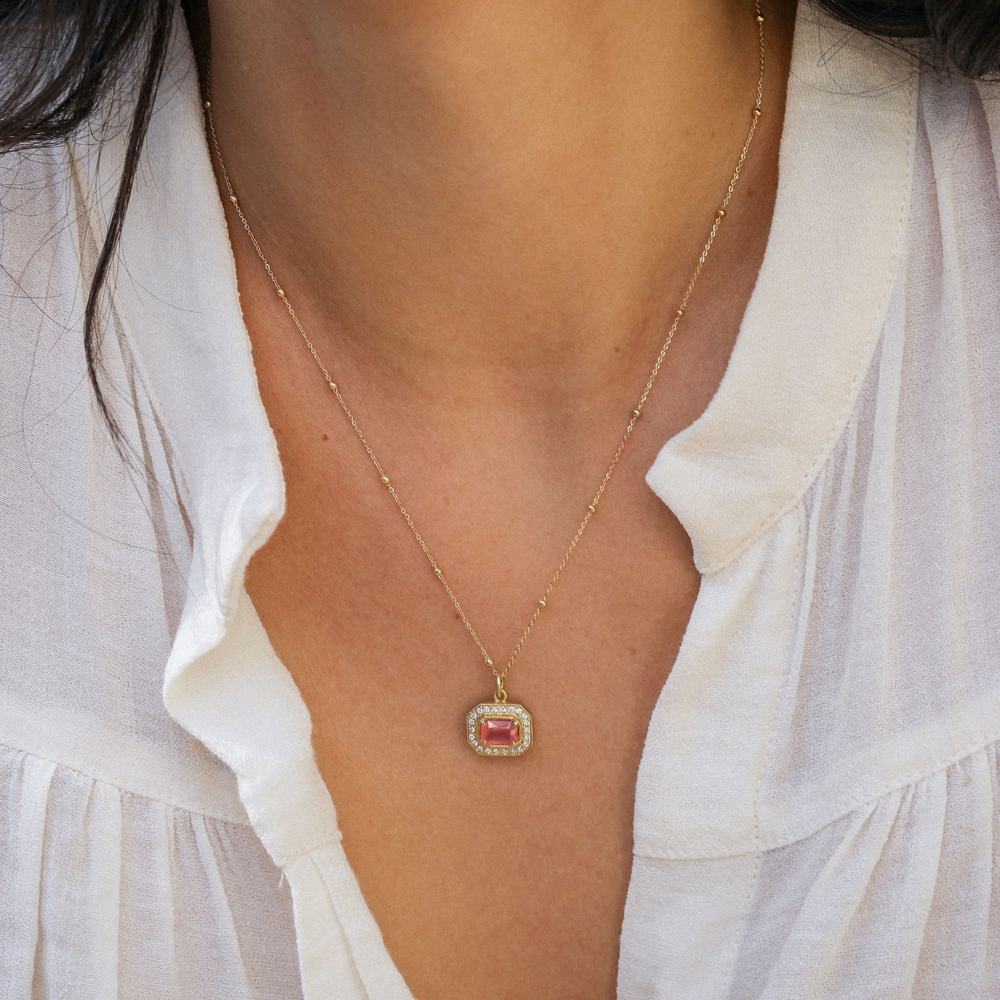 close up of a girl wearing a rhodochrosite pendant necklace with white diamond pave detailing and an 18k gold beaded chain.