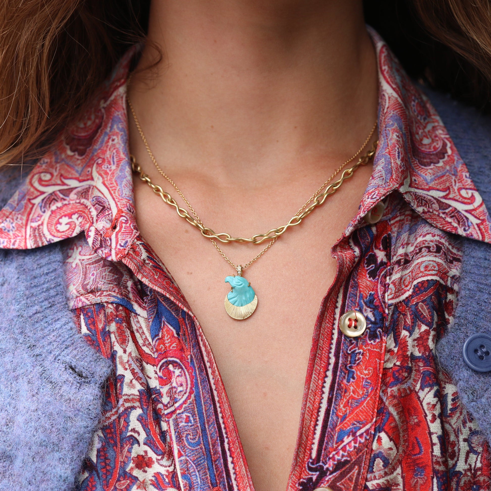 Person wearing a patterned shirt with a blue jacket and gold necklace with a turquoise eagle pendant.