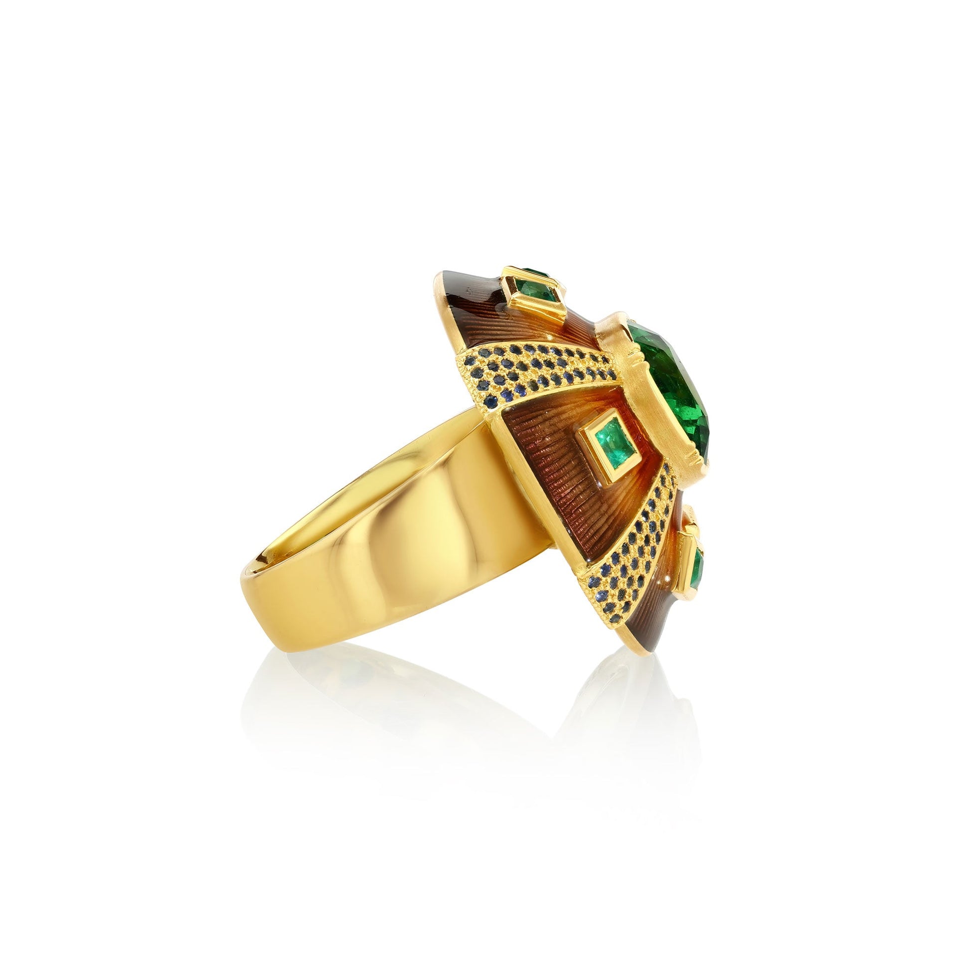 side view of decorative ring with green tsavorites and emeralds and blue sapphires with enameling and engraving on a white background.