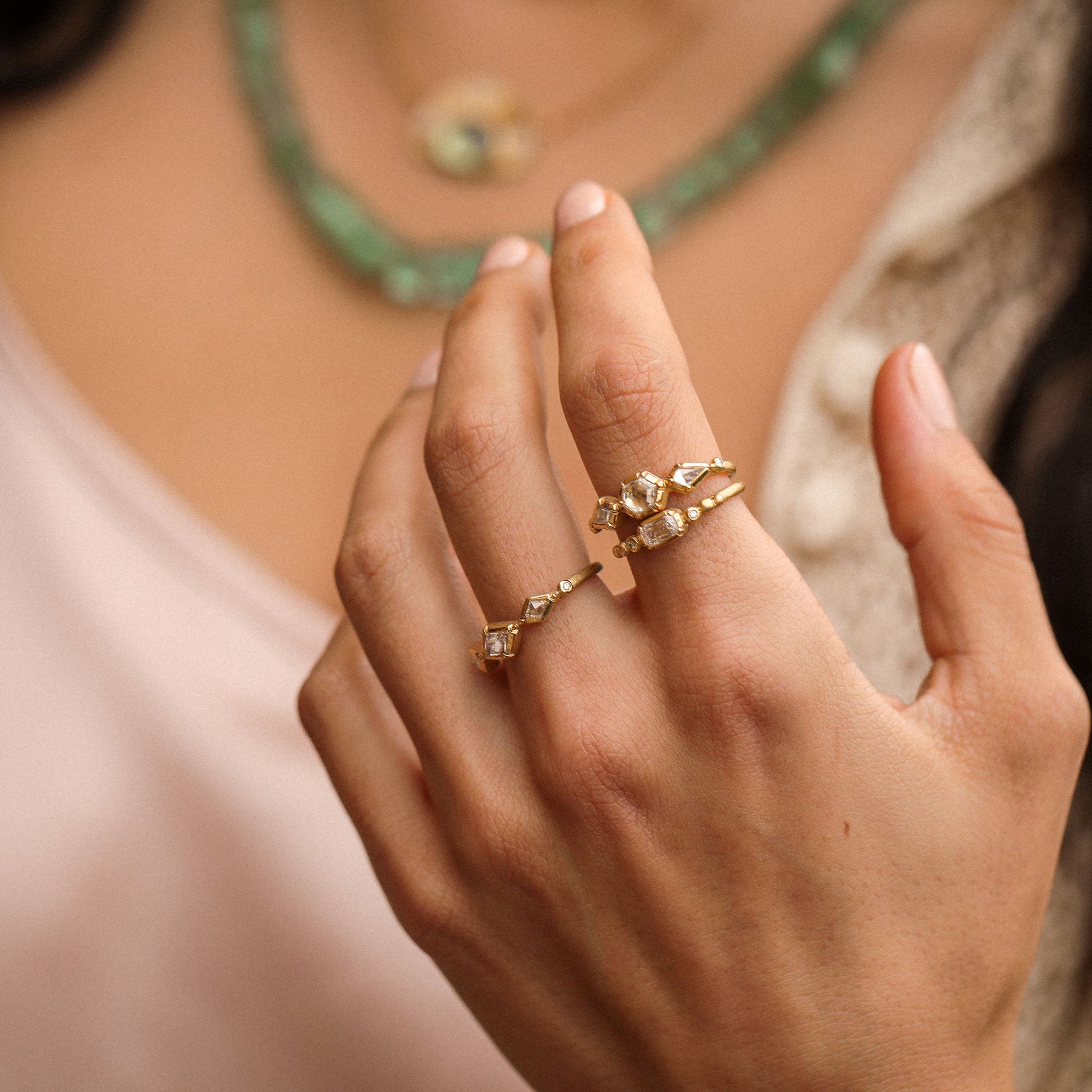 Close-up of a hand wearing a gold ring with gemstones, with a blurred background.