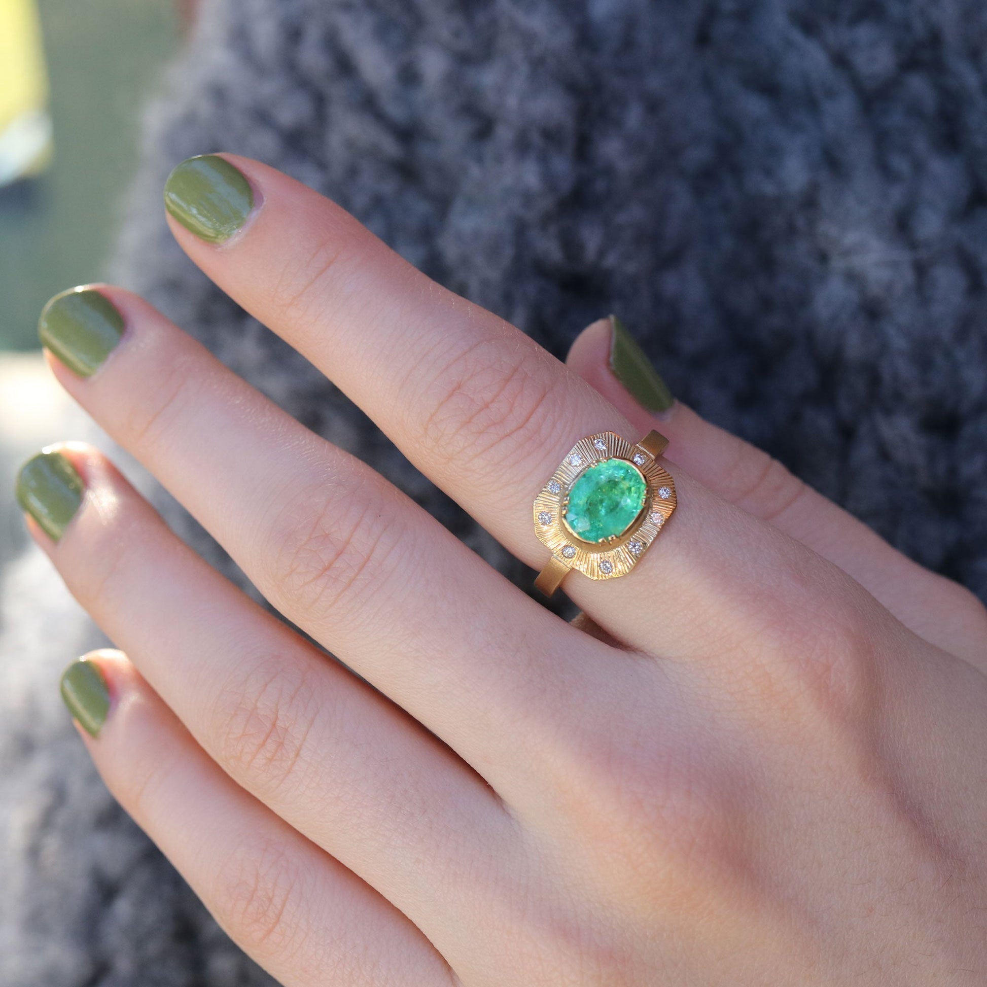 Hand wearing a goldring with a green paraiba gemstone against a blurred background