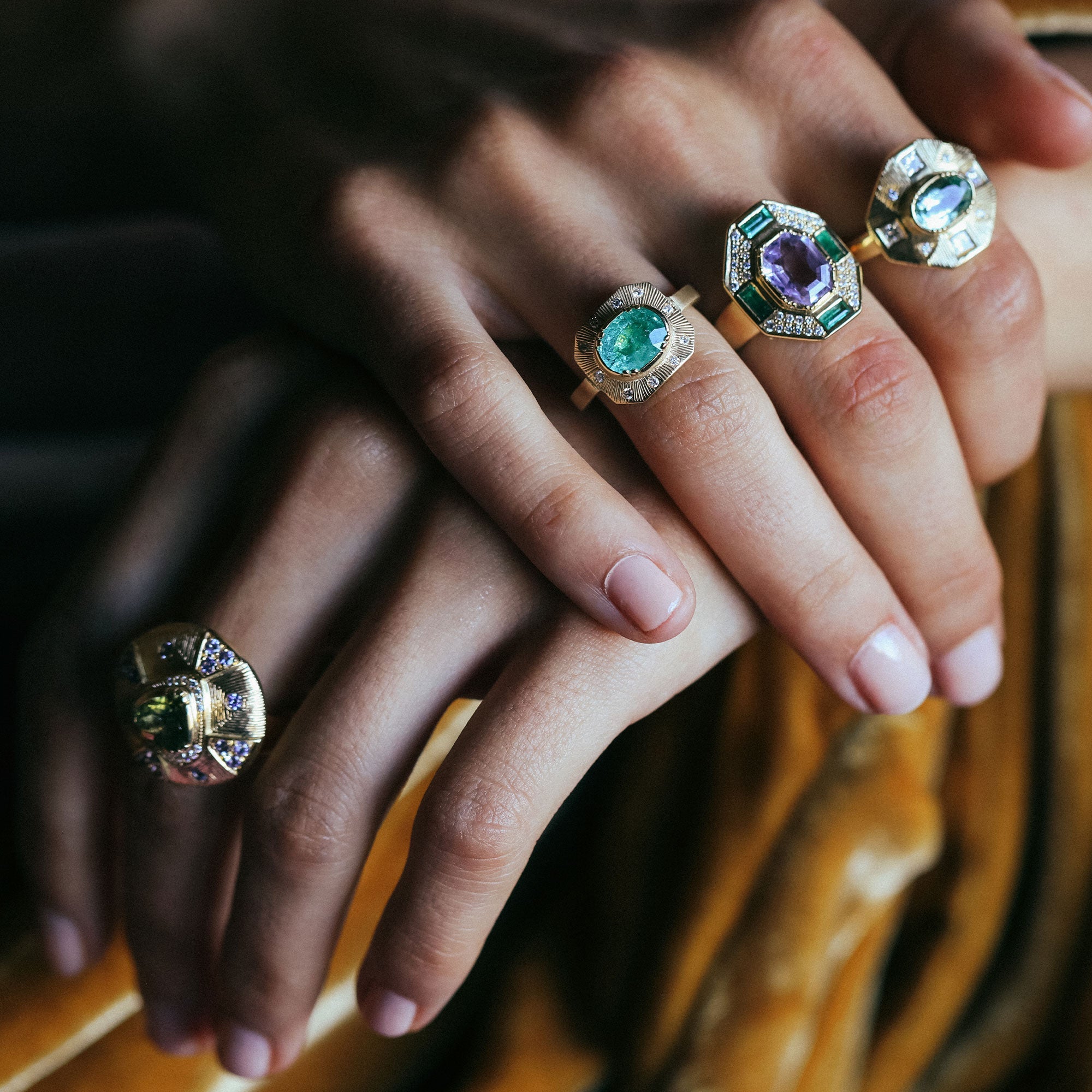 Close-up of hands wearing gold rings with gemstones on a blurred background
