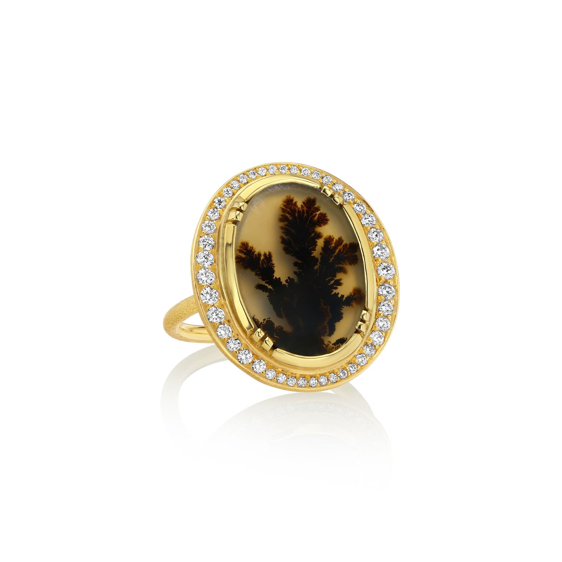 An 18k gold ring featuring an oval dendritic agate stone with a dark brown to black dendritic pattern, surrounded by a halo of small white diamond stones, set against a plain white background with a soft reflection.