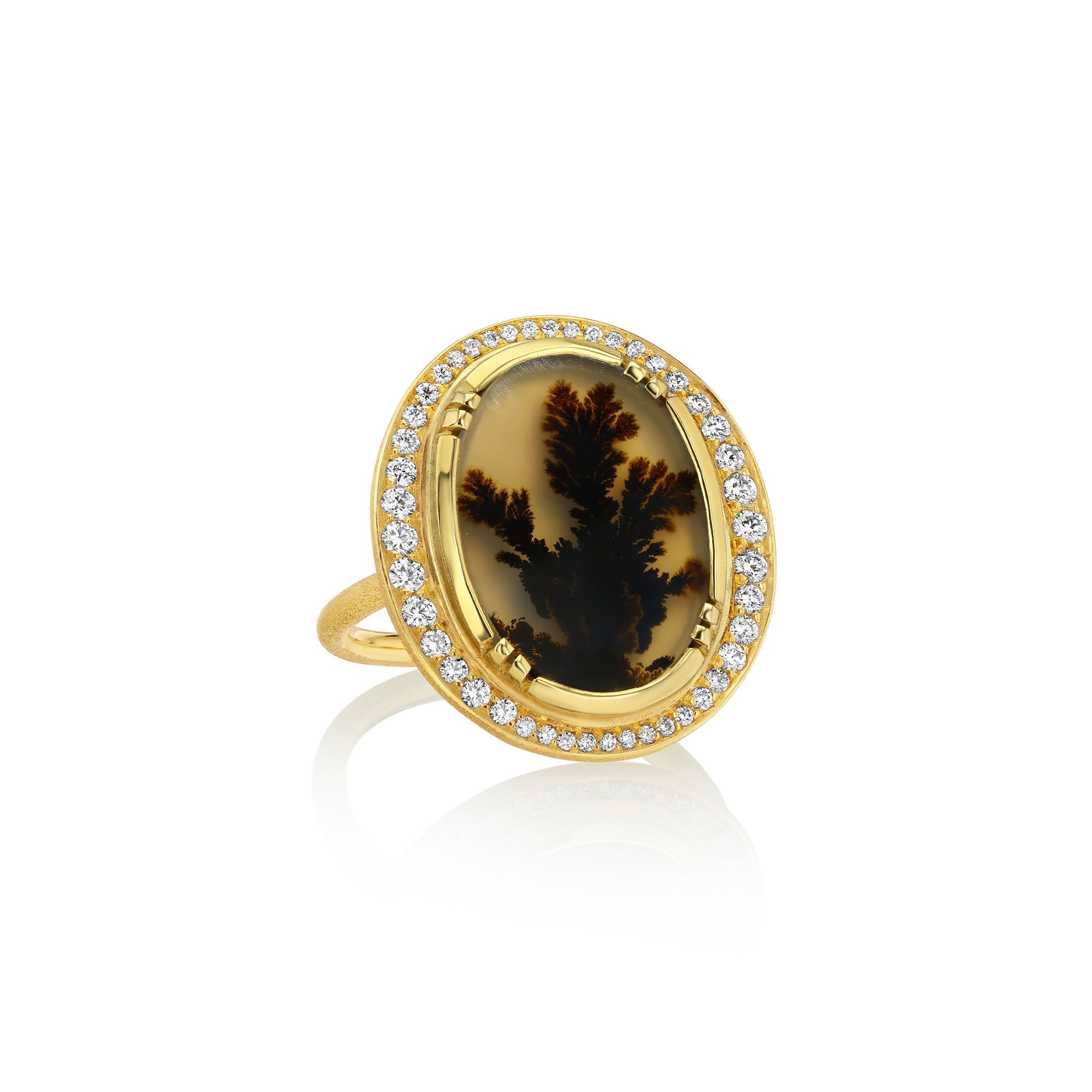 An 18k gold ring featuring an oval dendritic agate stone with a dark brown to black dendritic pattern, surrounded by a halo of small white diamond stones, set against a plain white background with a soft reflection.